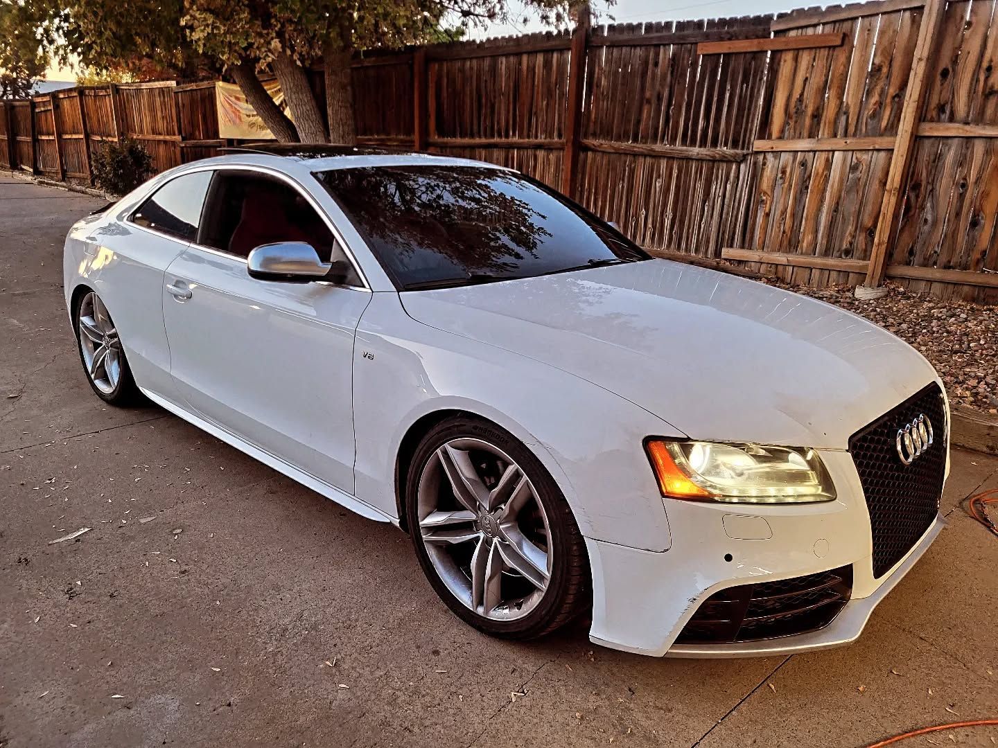 White Audi sedan parked on a driveway beside a wooden fence at dusk