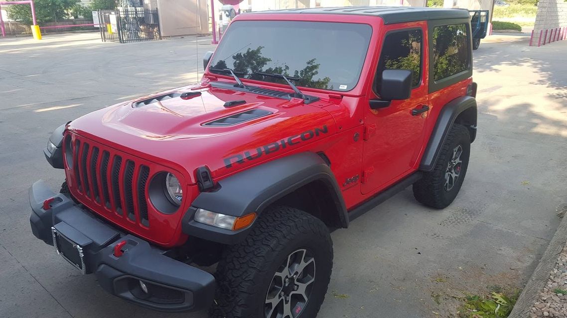 Red Jeep Wrangler parked on a street, angled front-left, with a black roof and off-road tires.