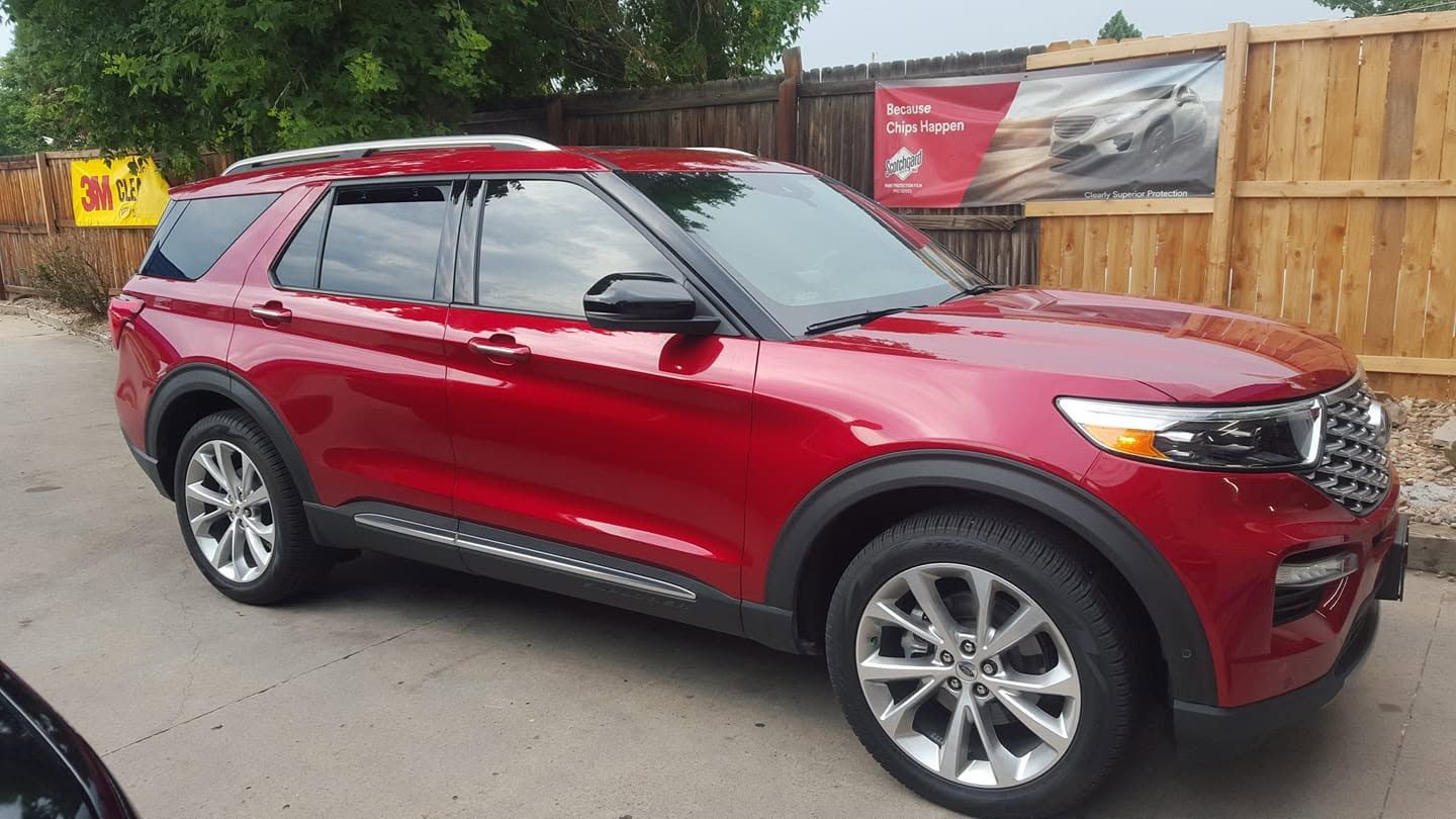 Red SUV parked beside a wooden fence on a wet street.