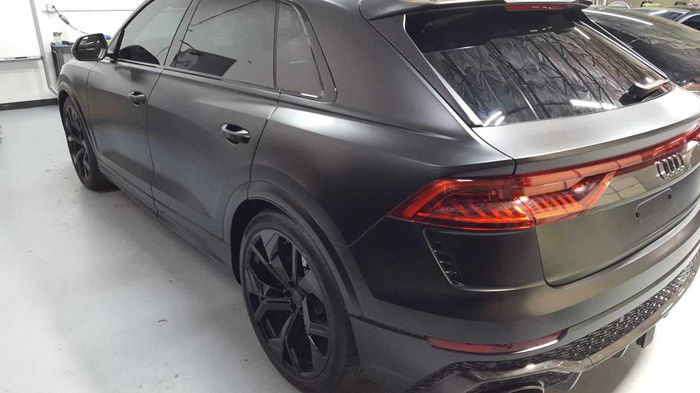 Matte black SUV in a studio, rear three-quarter view with tinted windows and red taillights.