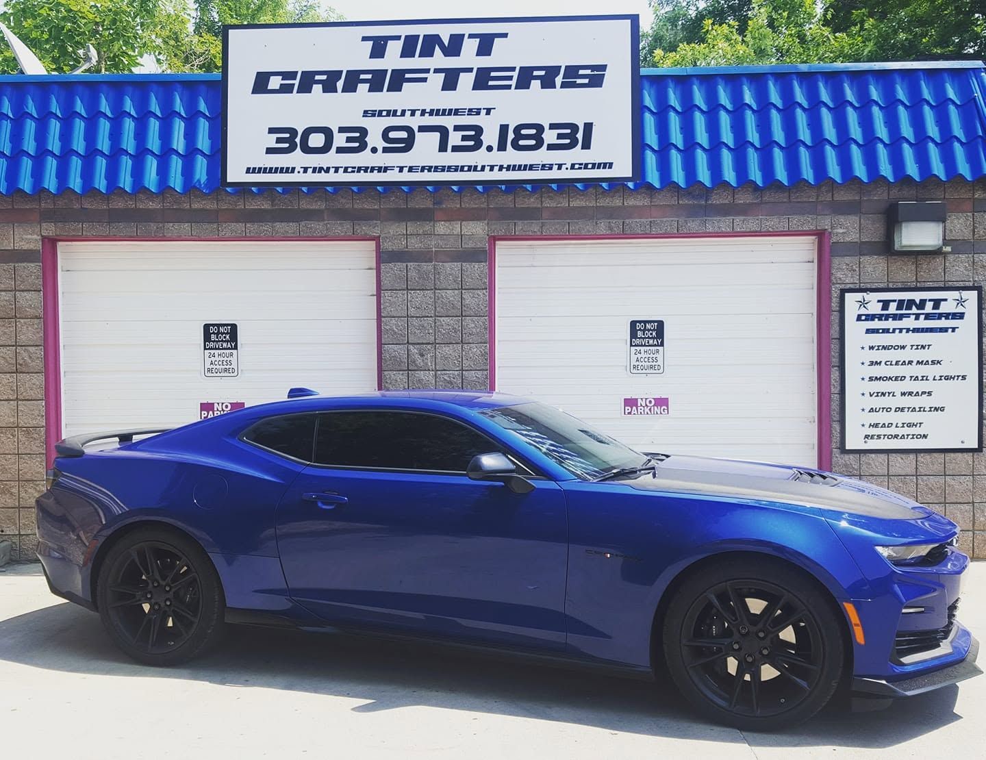 Blue sports car parked outside Tint Grafters shop with blue roof and white garage doors.