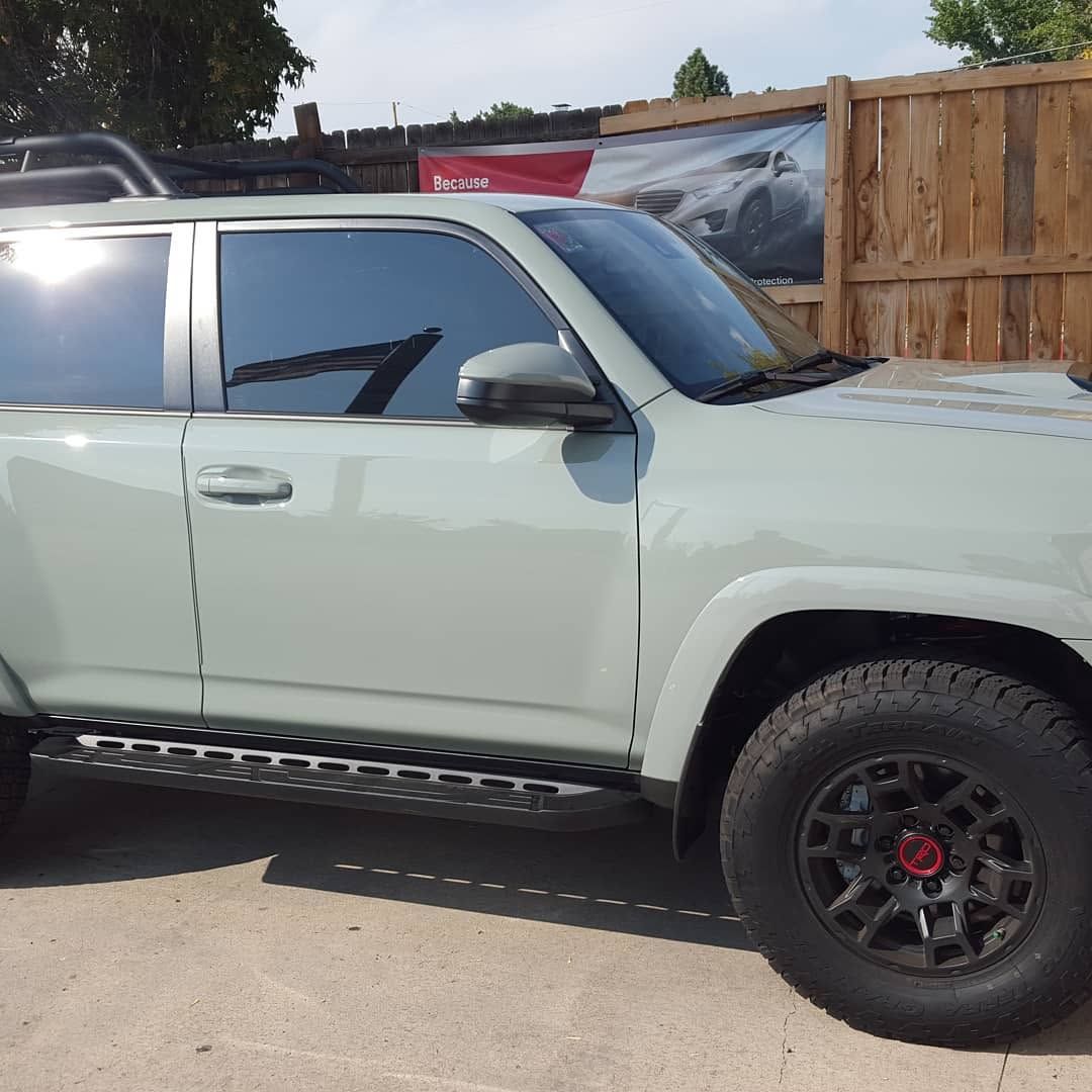 Light green pickup truck with black off-road wheels parked beside a wooden fence.