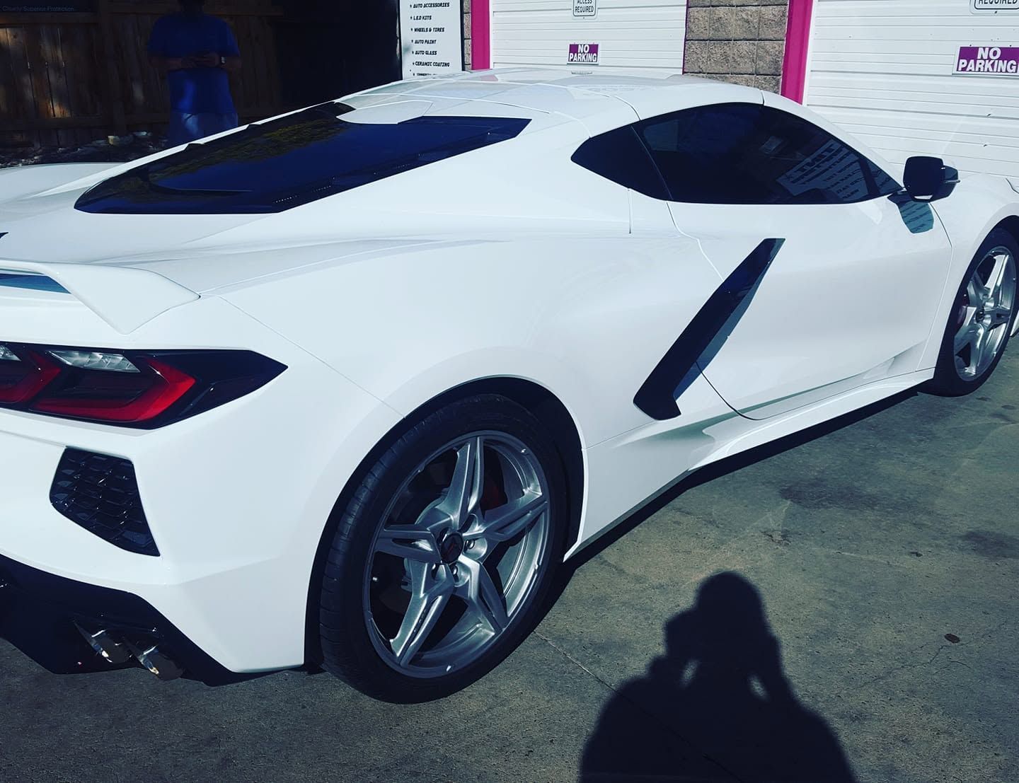 White sports car parked outside a building, rear-side view with dark tinted windows and shadow on pavement