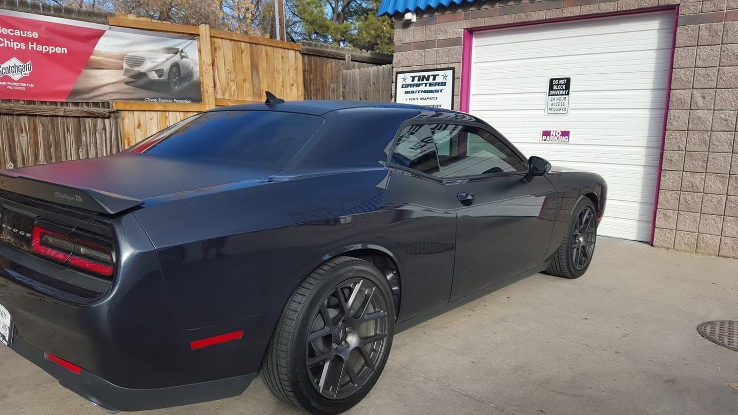Black sports car parked beside a garage door in a driveway, rear three-quarter view