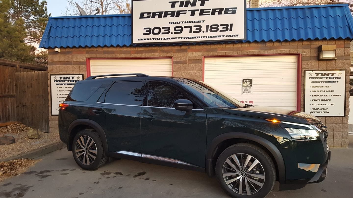 Dark SUV parked outside Tint Drifters auto shop with blue roof and garage doors