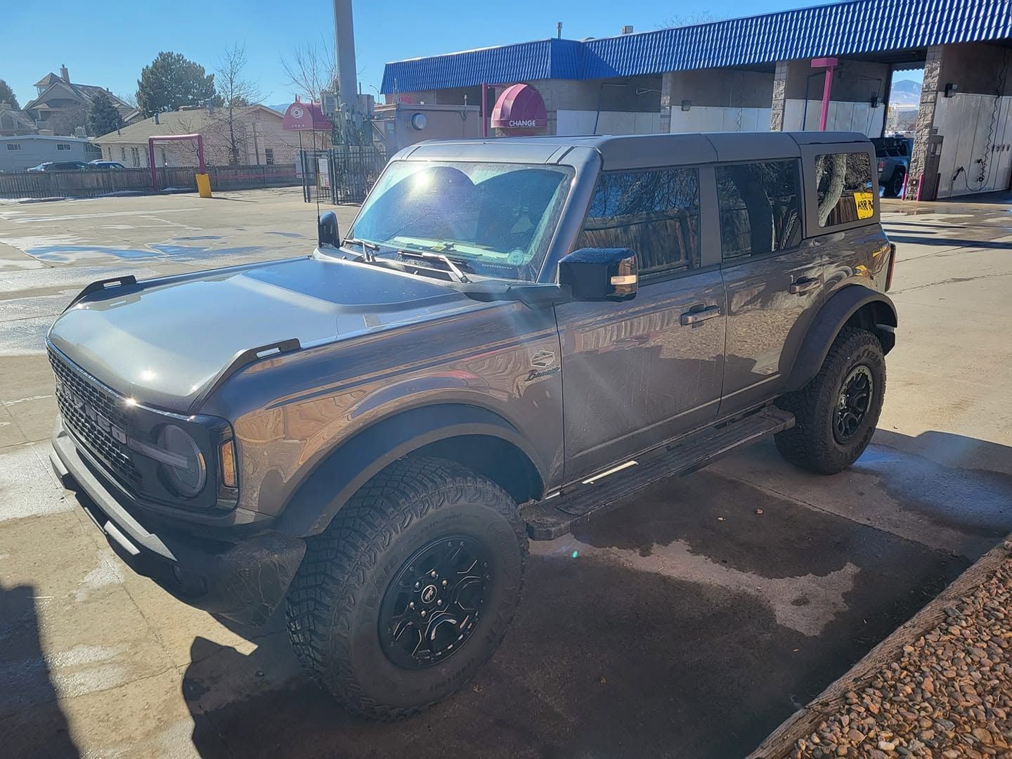Black off-road SUV parked on a dirt lot beside a blue-roofed building, muddy and sunlit.