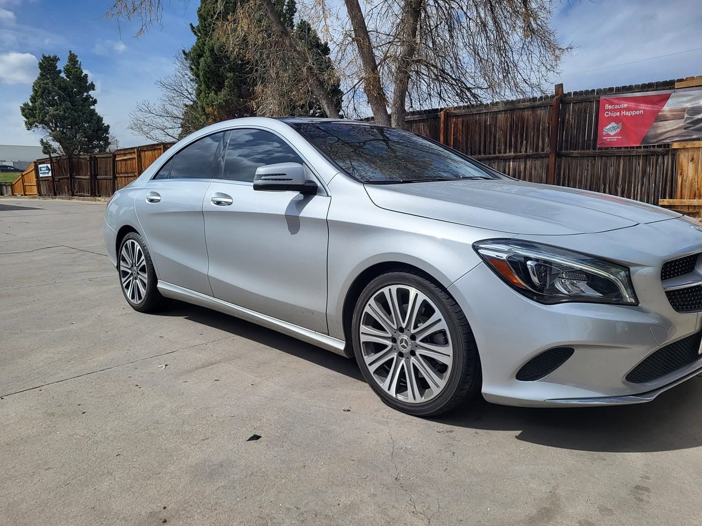 Silver sedan parked on a sunny driveway beside a wooden fence and trees