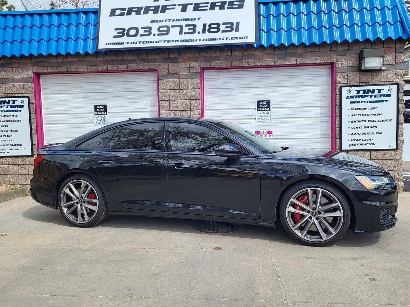 Black sports sedan parked in front of a blue-roof auto shop with garage doors