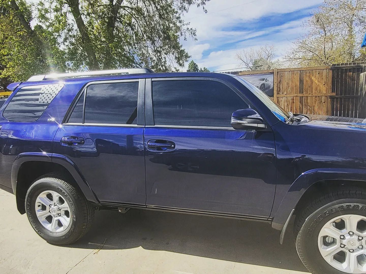 Dark blue SUV parked outdoors beside a wooden fence under a partly cloudy sky
