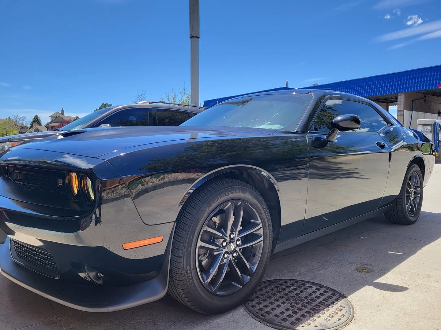 Black sports car parked outdoors in sunlight, front-left view, with blue-tinted windshield and black rims