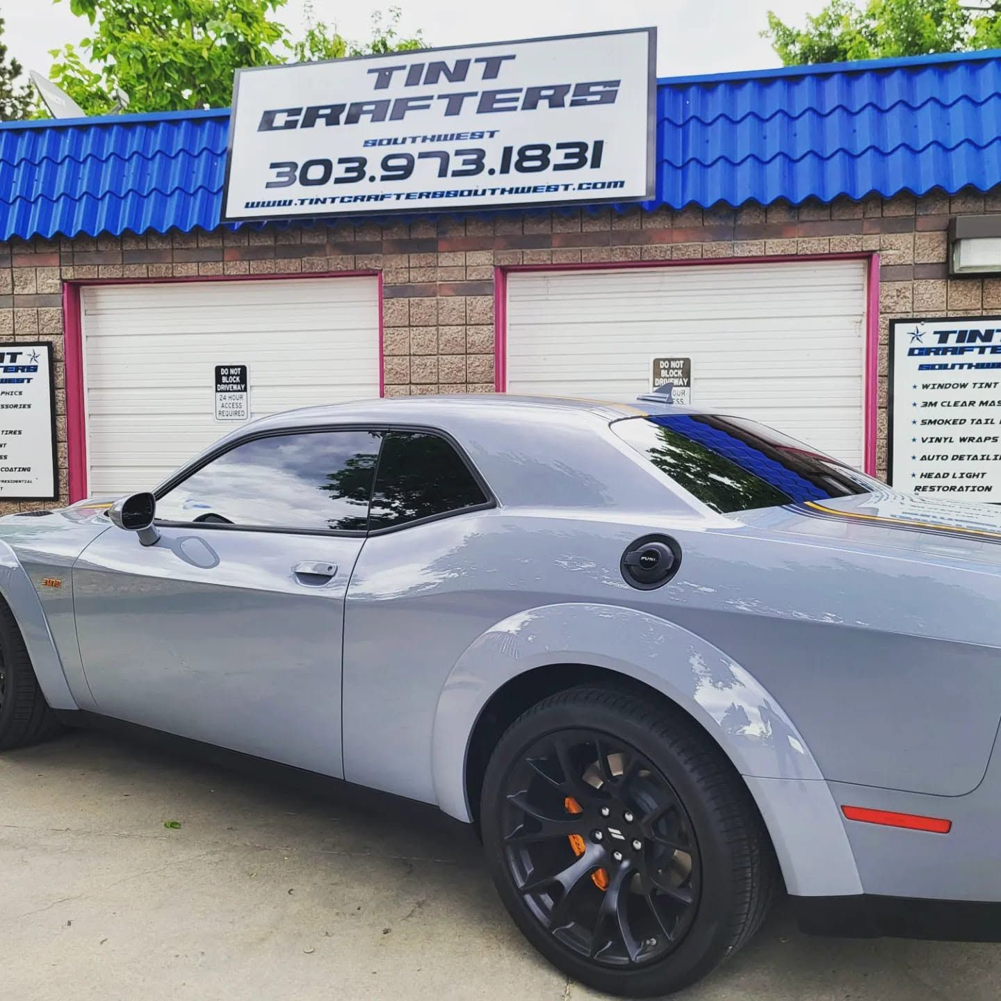 Gray sports car parked outside Tint Masters shop with blue roof and closed white garage doors