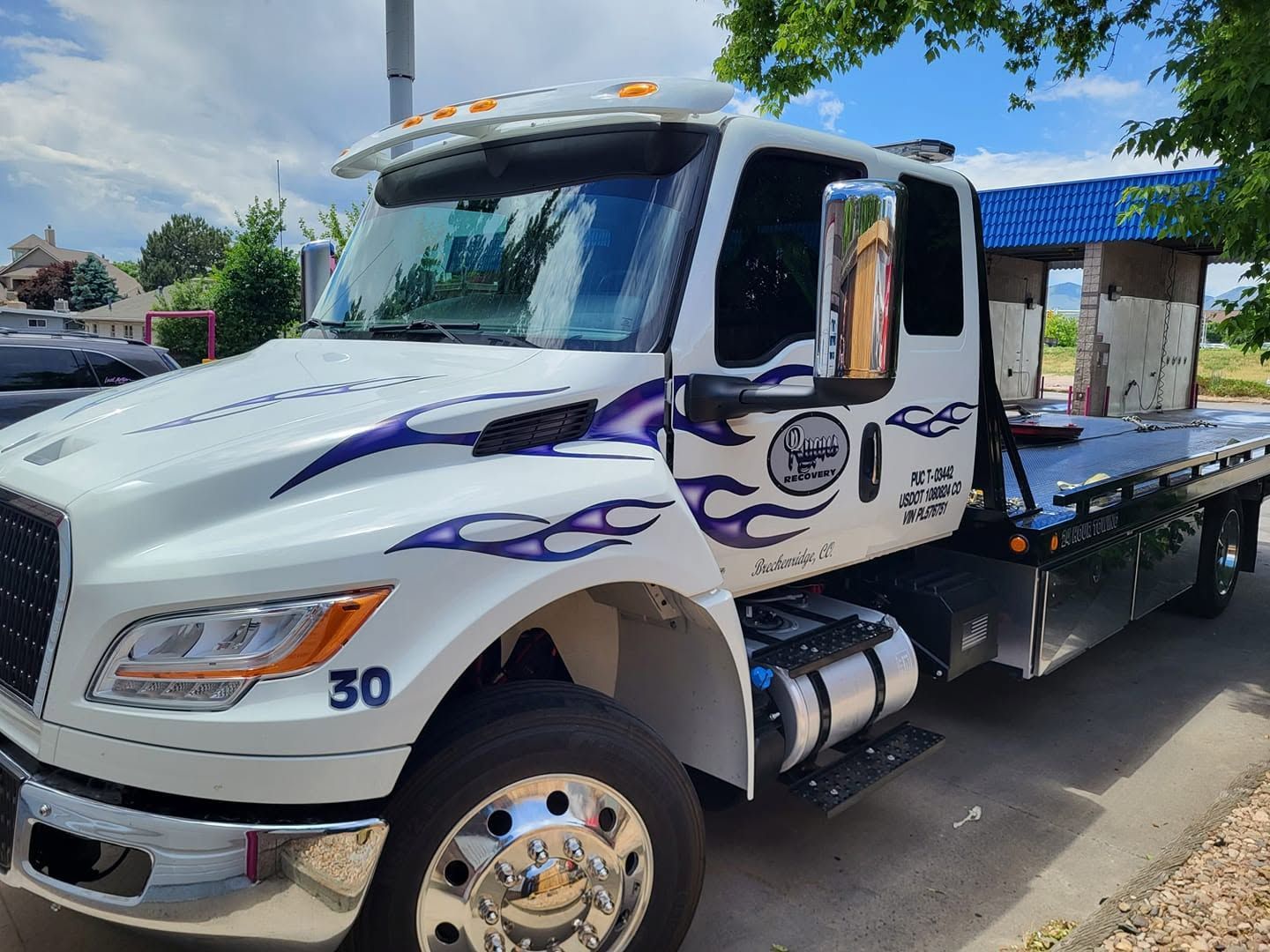 White flatbed tow truck with purple flames parked outdoors under a blue canopy