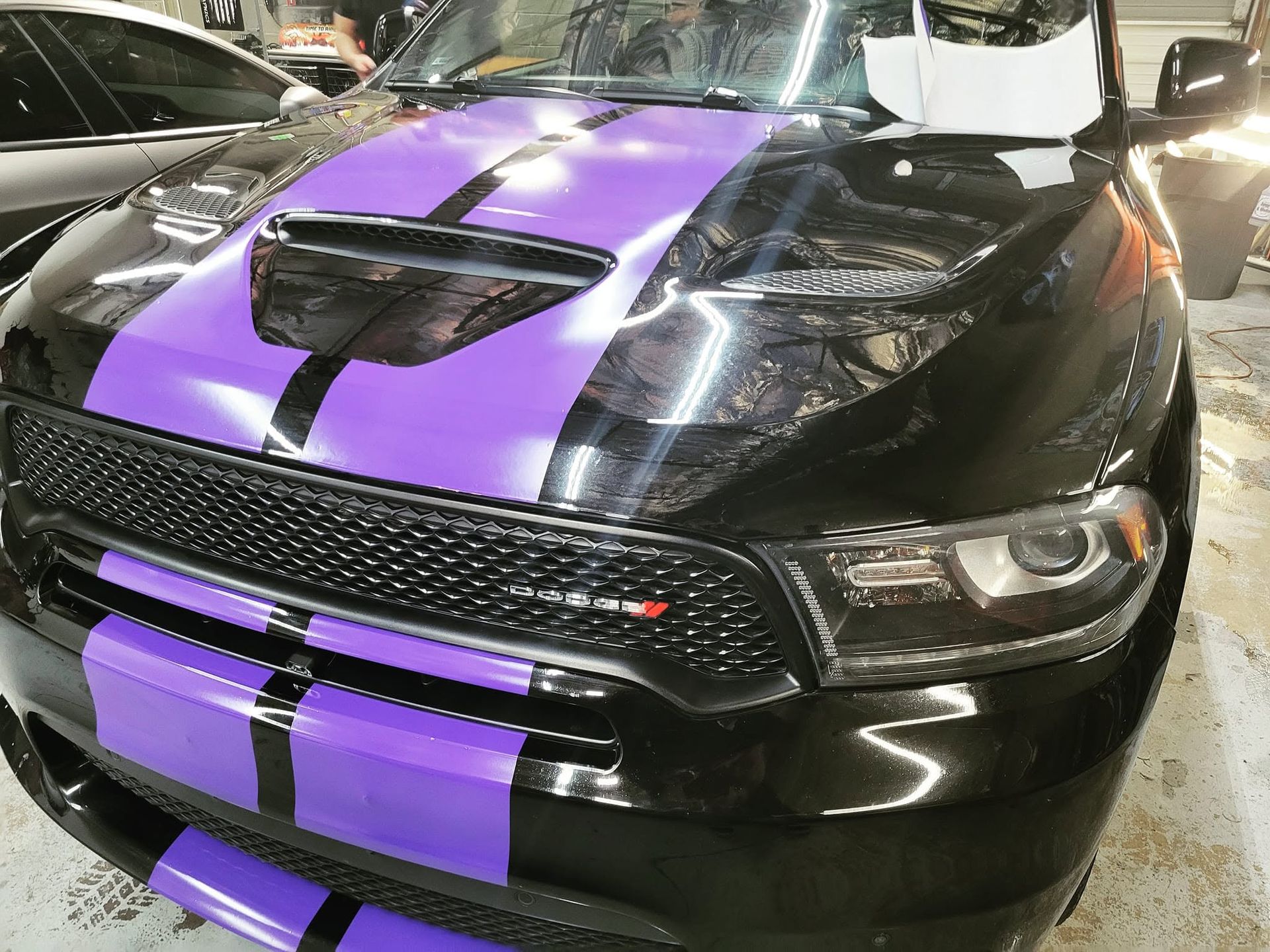 Black muscle car with purple racing stripes parked indoors
