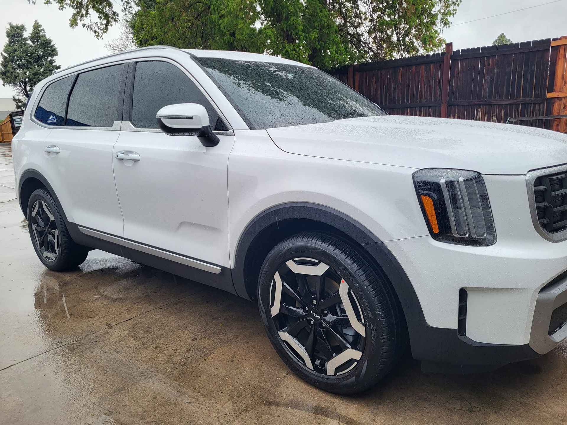 White SUV parked on a wet driveway, front-left view, with black wheels and tinted windows.