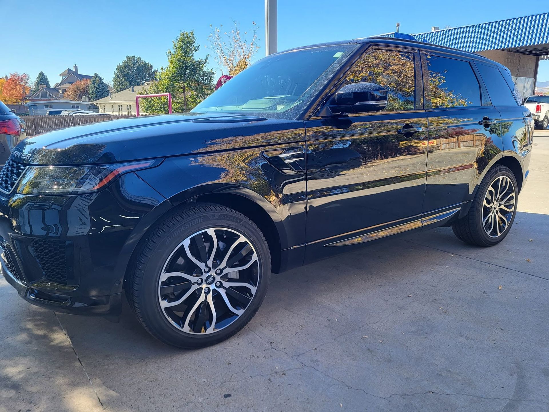 Black SUV parked outdoors on a sunny day, side view with trees reflected in the windows