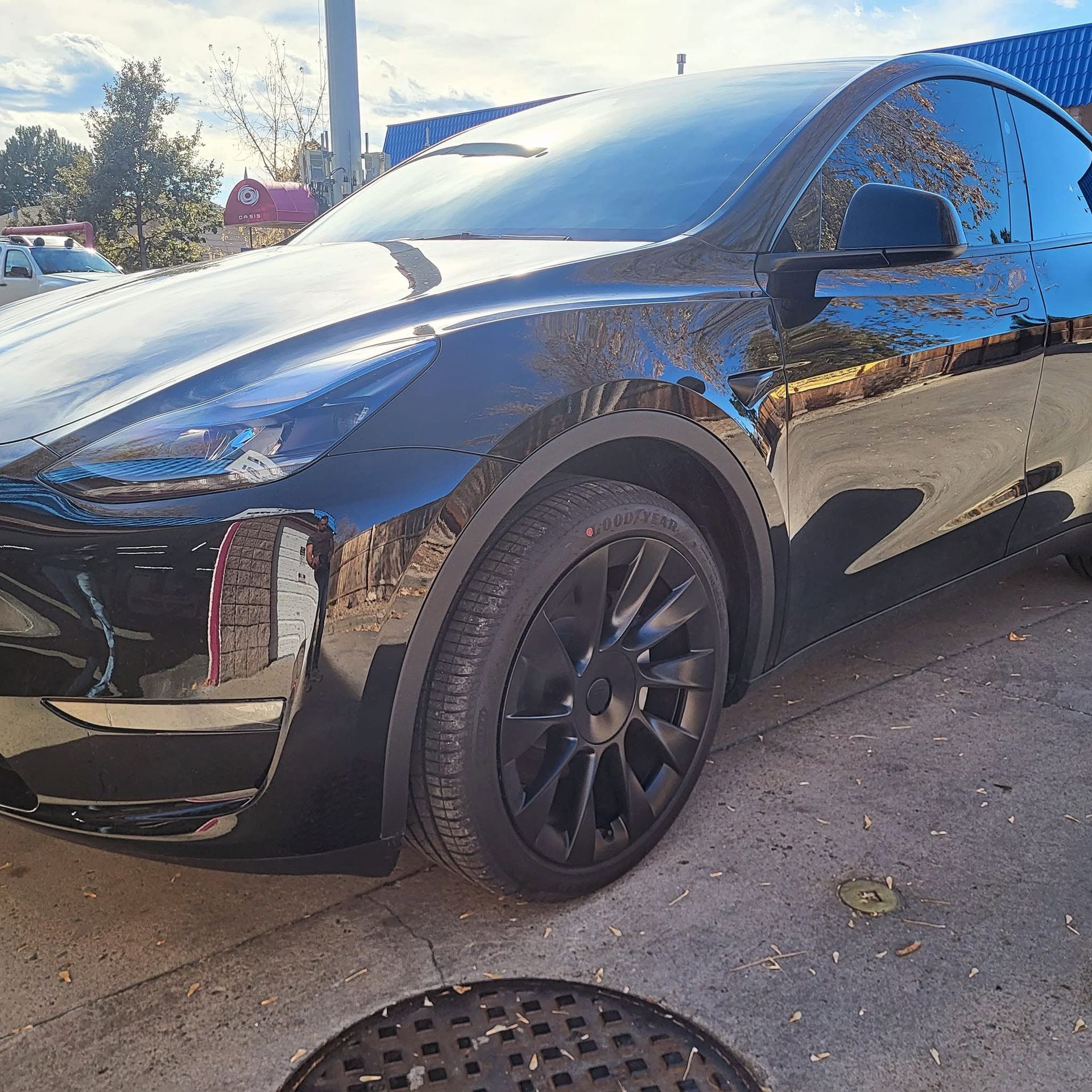 Black Tesla SUV parked outdoors in sunlight, front-left view, with black rims and a reflection on the glossy paint