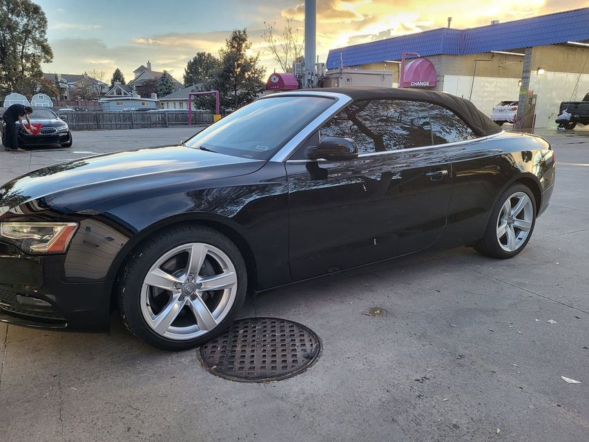 Black convertible parked on a street near a gas station at dusk