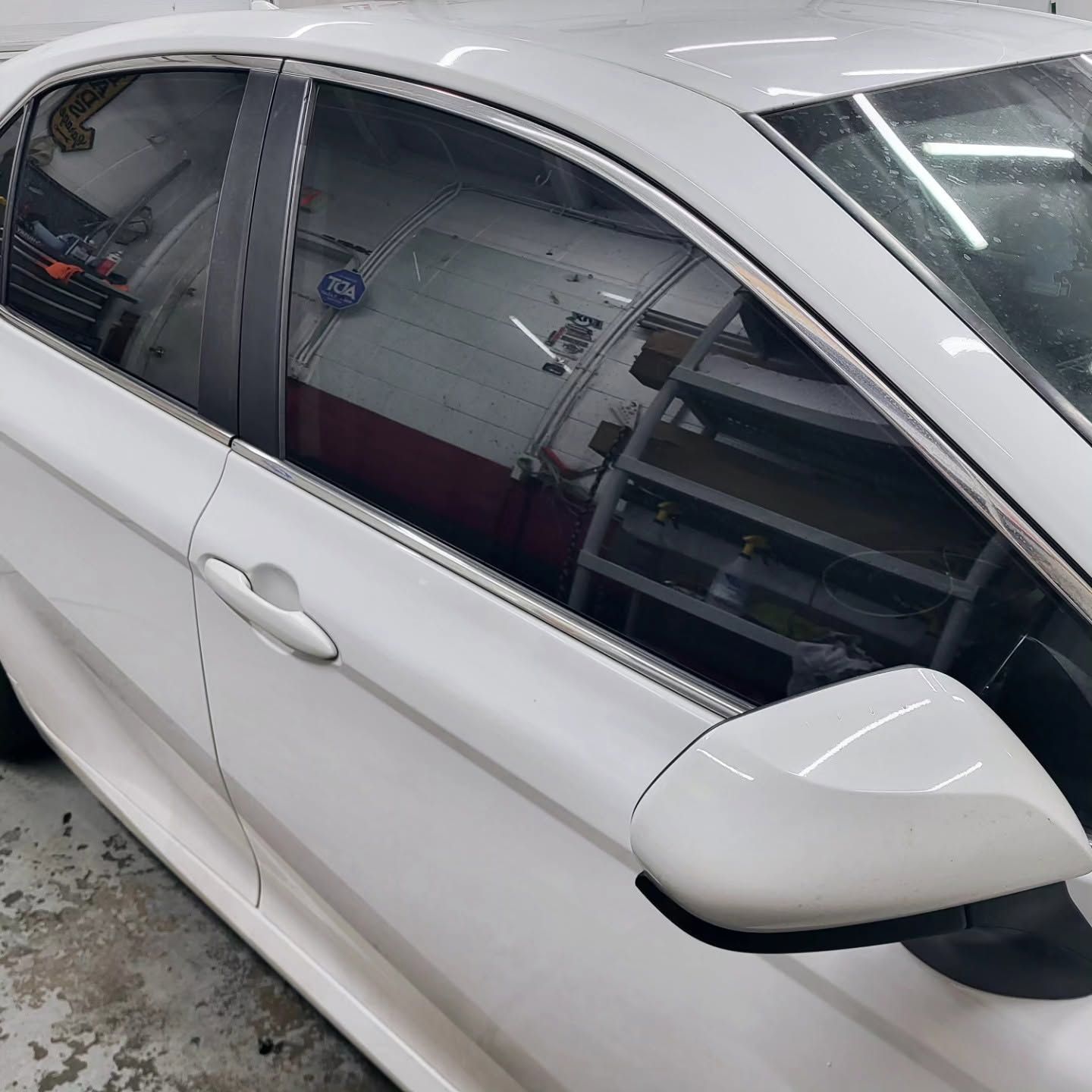 White sedan parked indoors, viewed from the side with tinted windows and a side mirror visible