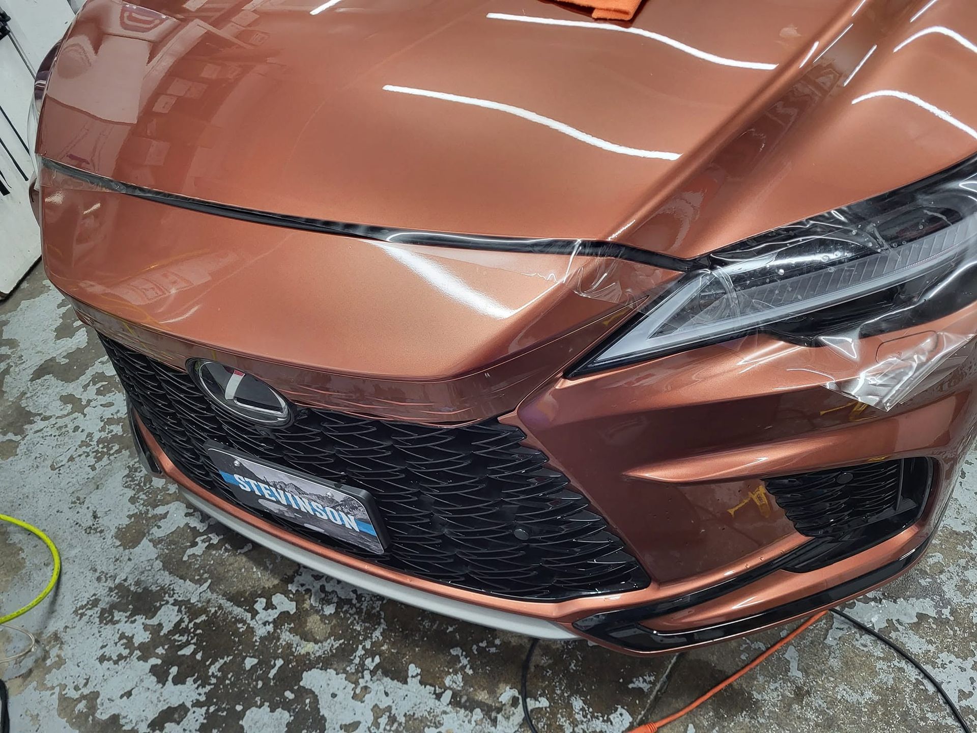 Copper-colored car front hood visibly damaged with a large dent in a garage or workshop.