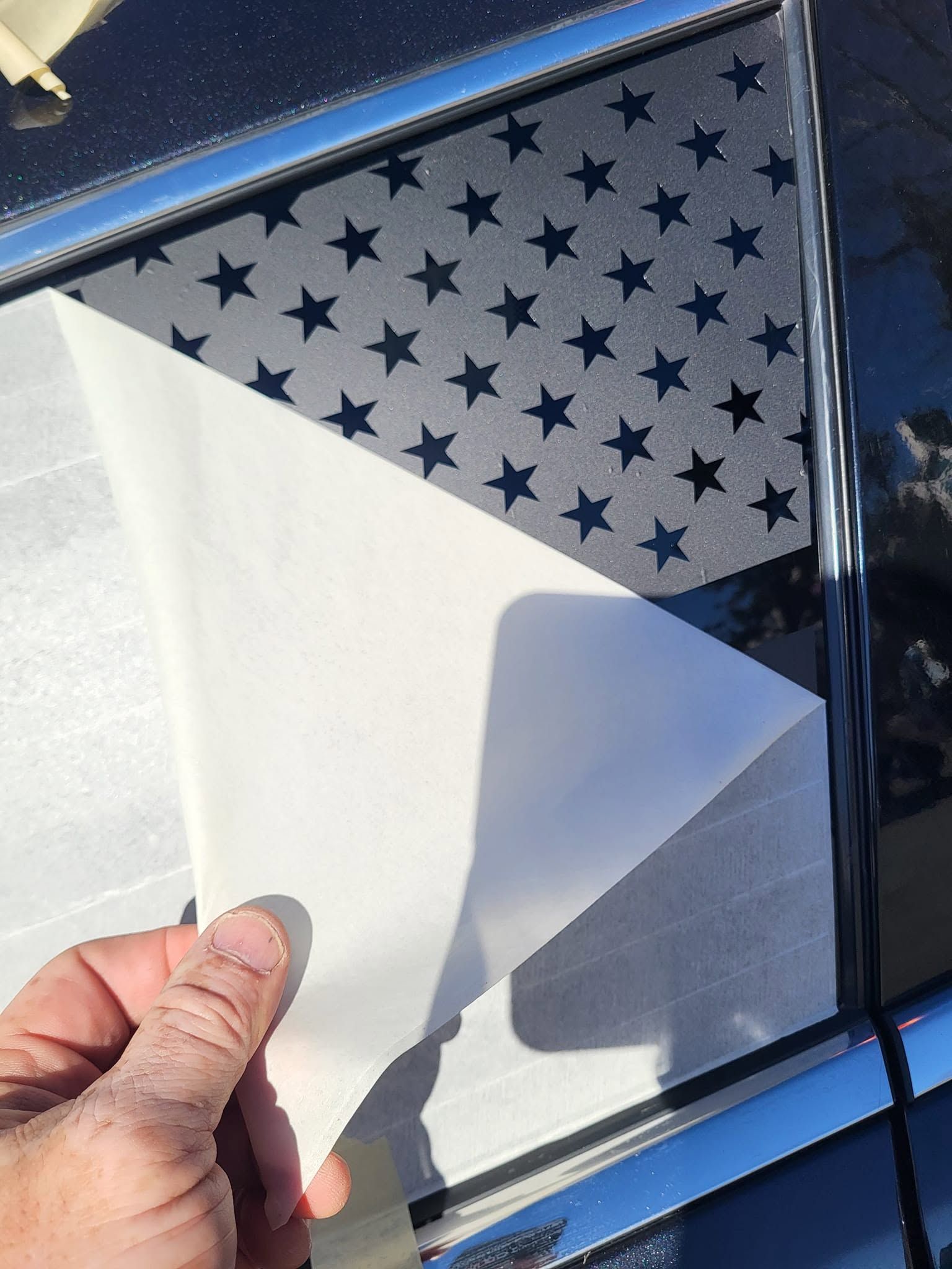 Hand peeling a white corner decal from a dark blue car window with star-patterned film underneath