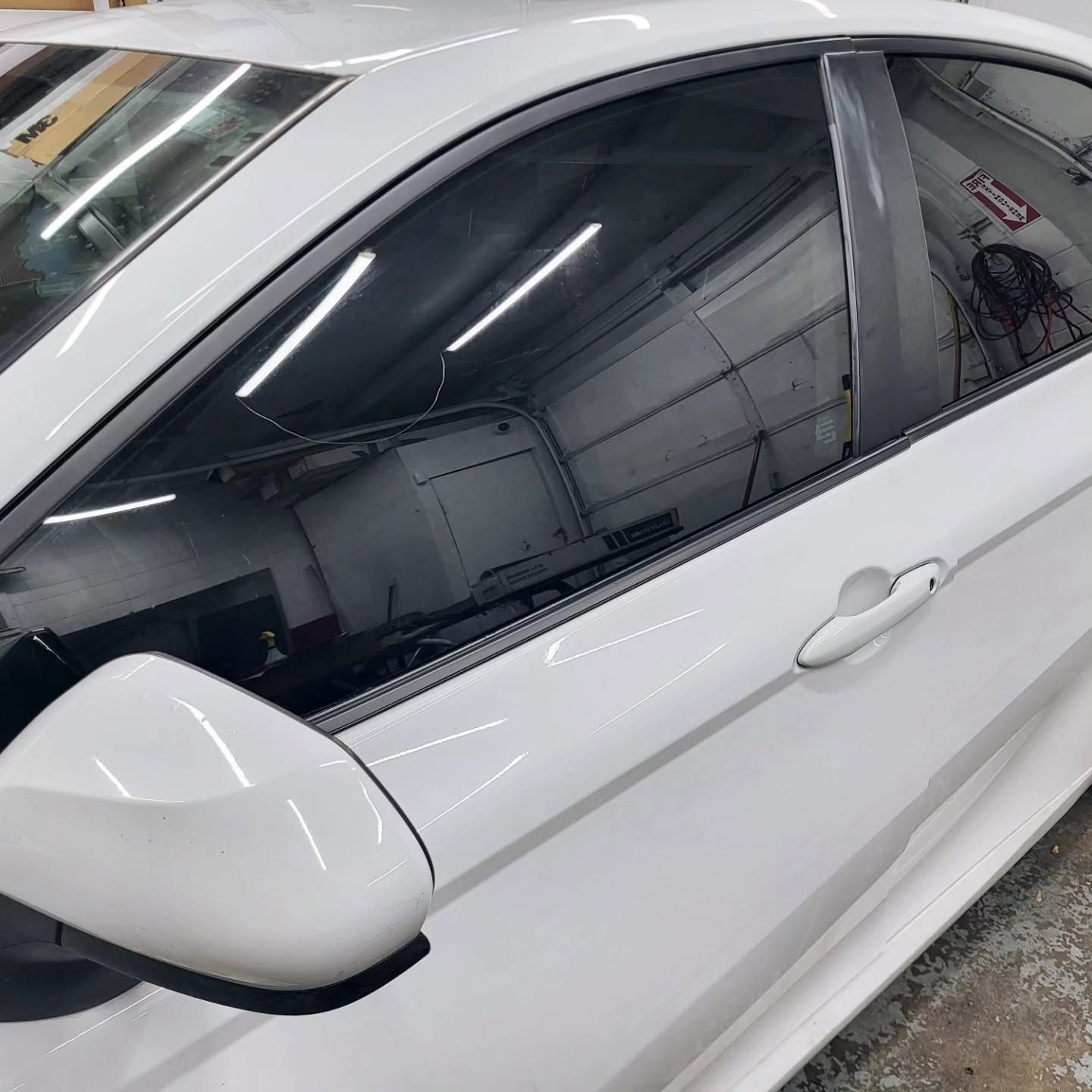 White car side with tinted windows and side mirror in a garage