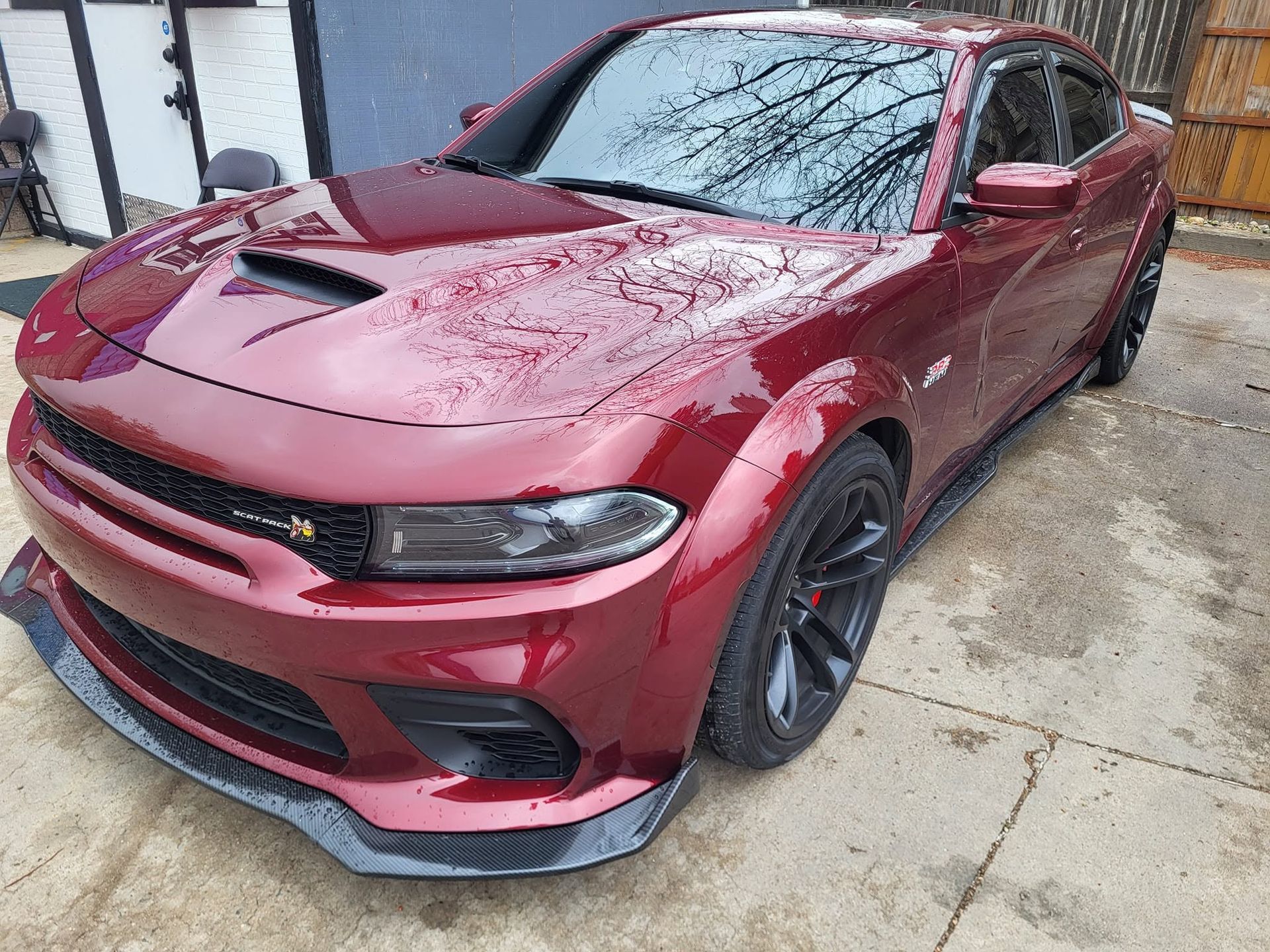 Red Dodge Charger parked on a wet driveway, viewed from the front-left side.