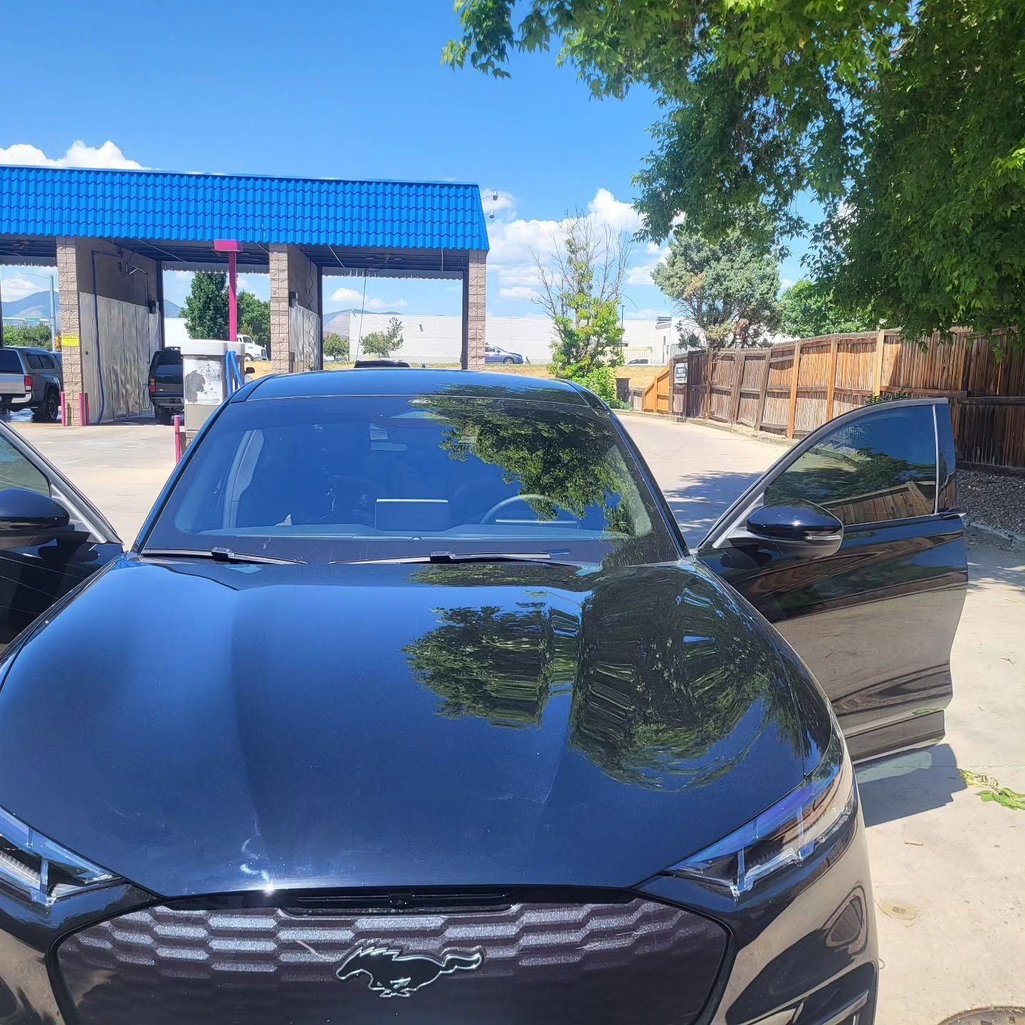 Black Chevrolet sedan with open doors parked at a blue-roofed station under a tree.