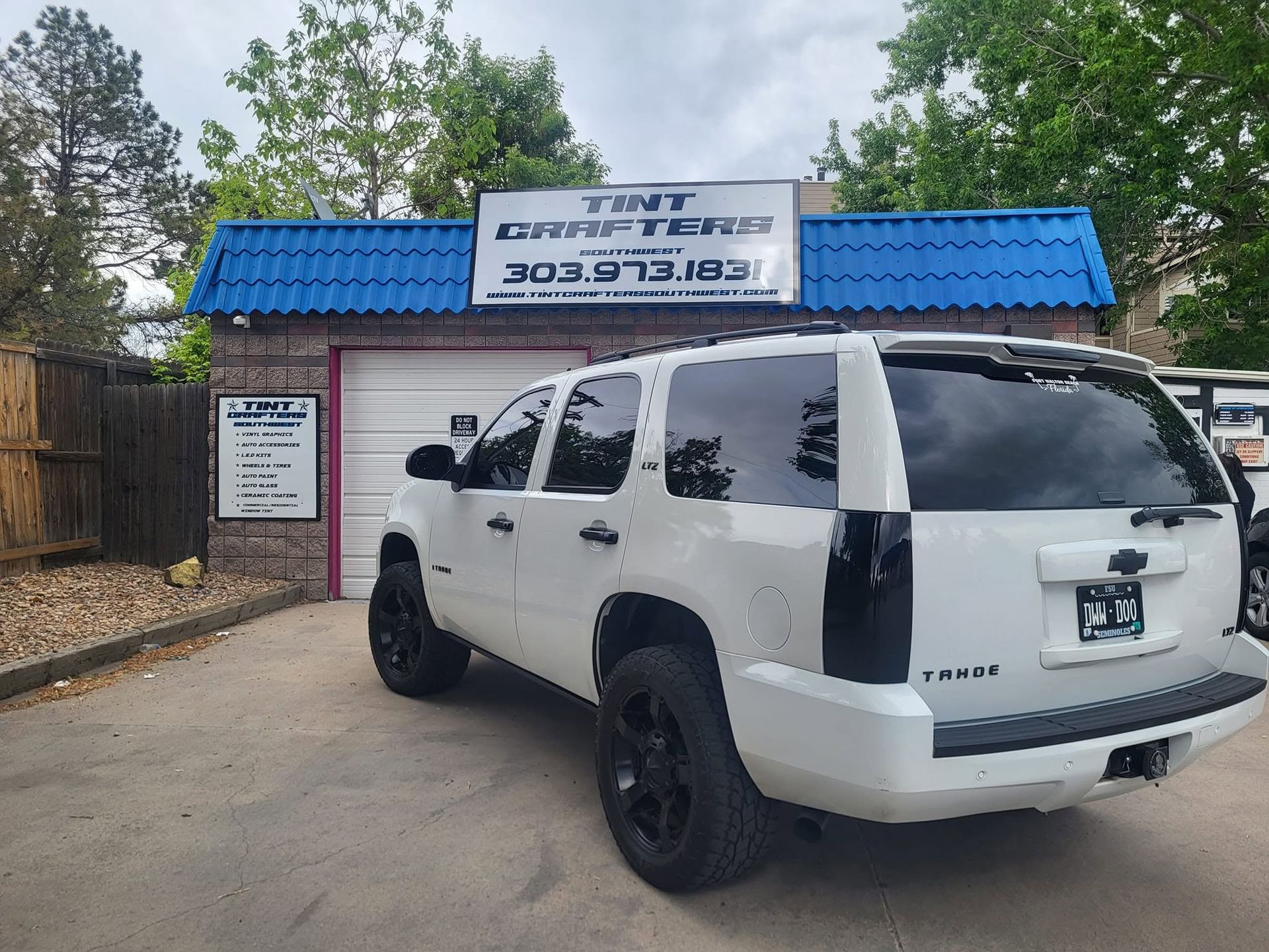 White SUV parked outside a small business with a blue roof and sign above the entrance.