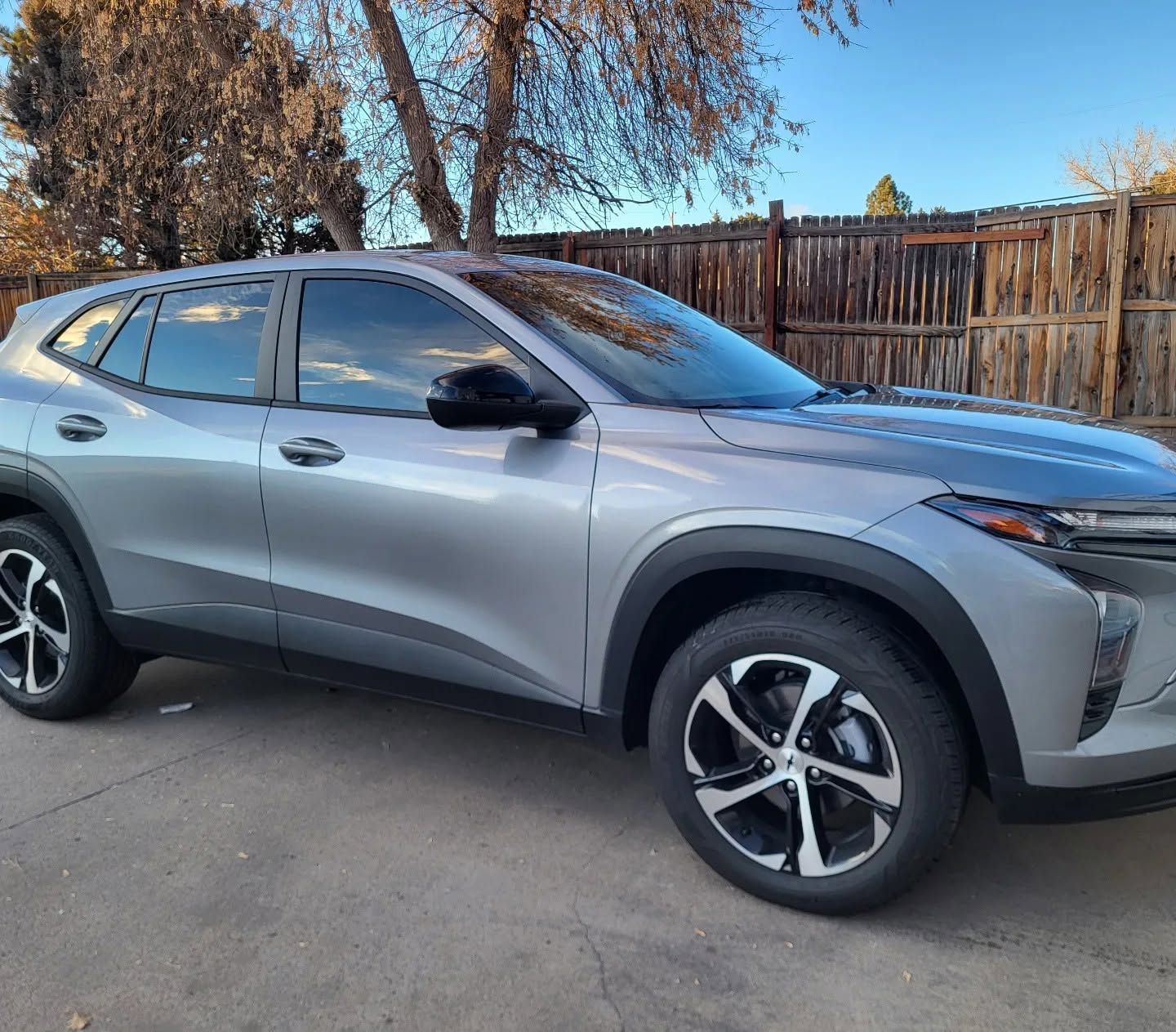 Silver SUV parked on a driveway beside a wooden fence under a clear sky