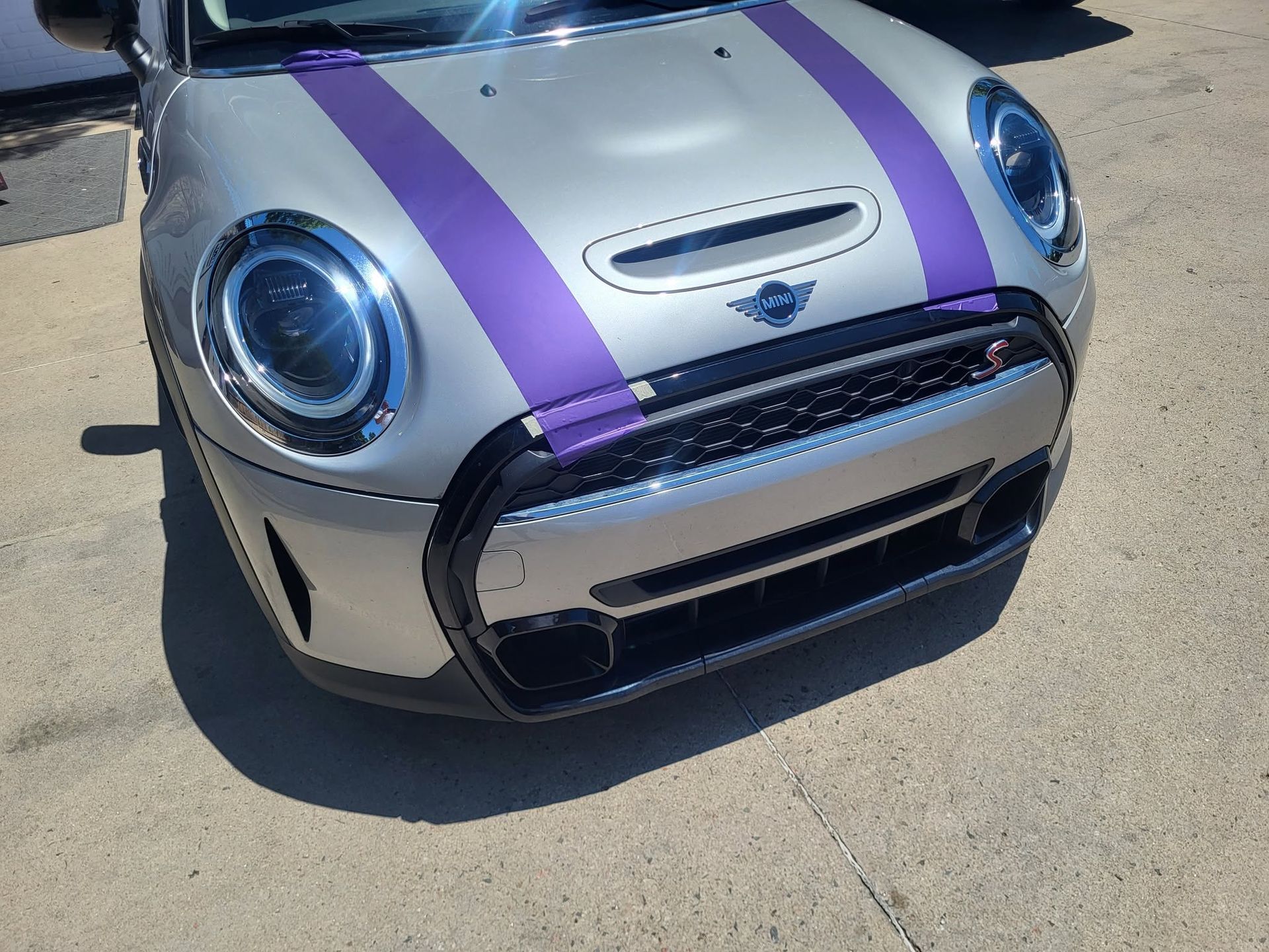 Silver Mini Cooper with purple racing stripes parked on pavement, front view