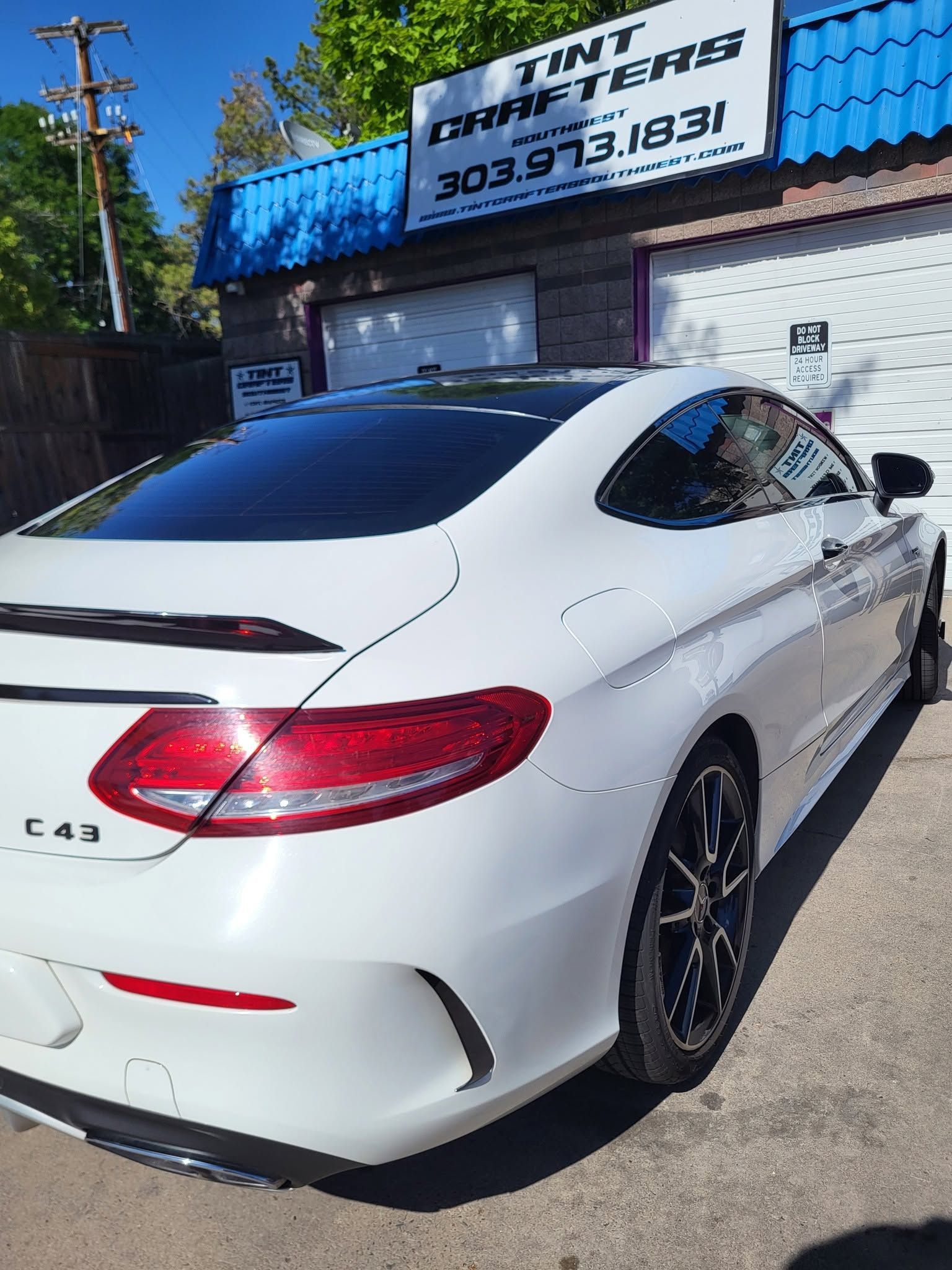 White Mercedes-Benz C43 coupe parked outside a tint shop with blue signage.