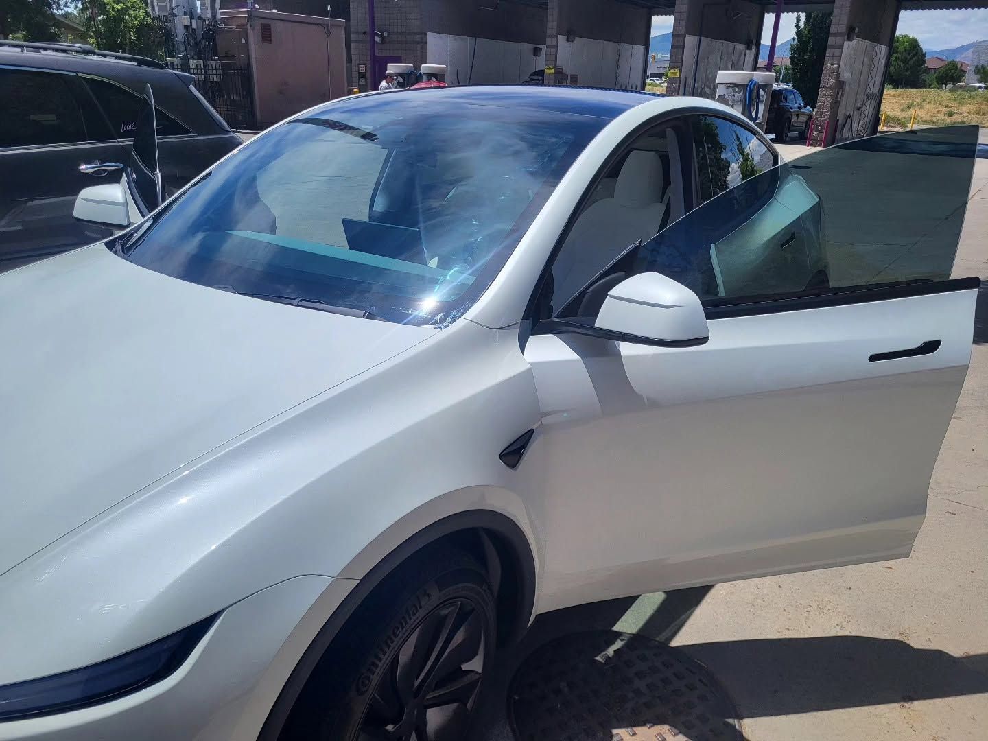 White Tesla with driver door open in a parking lot, with a dark car parked beside it.