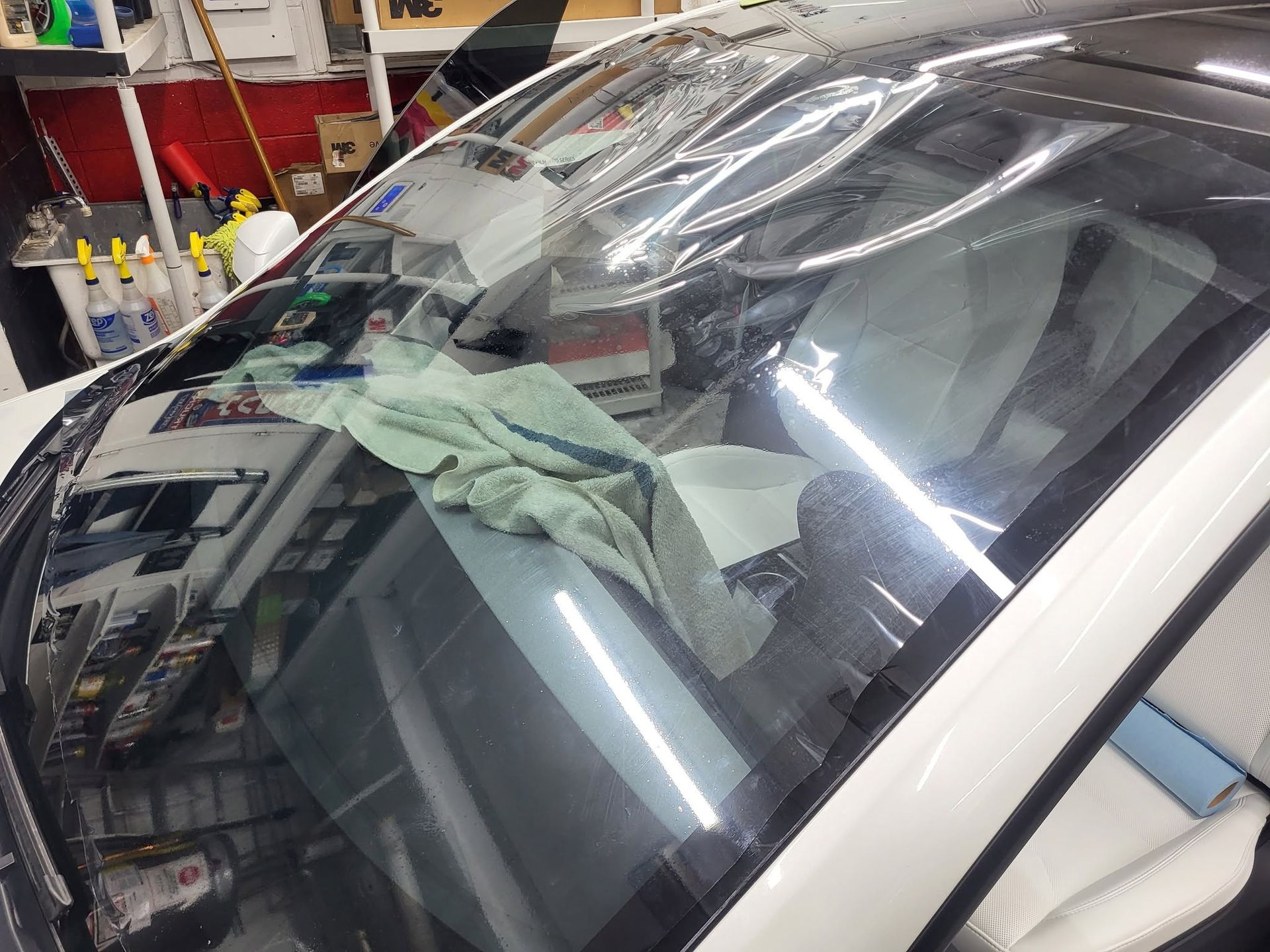 Windshield in an auto shop with a cloth draped inside, reflected under bright lights