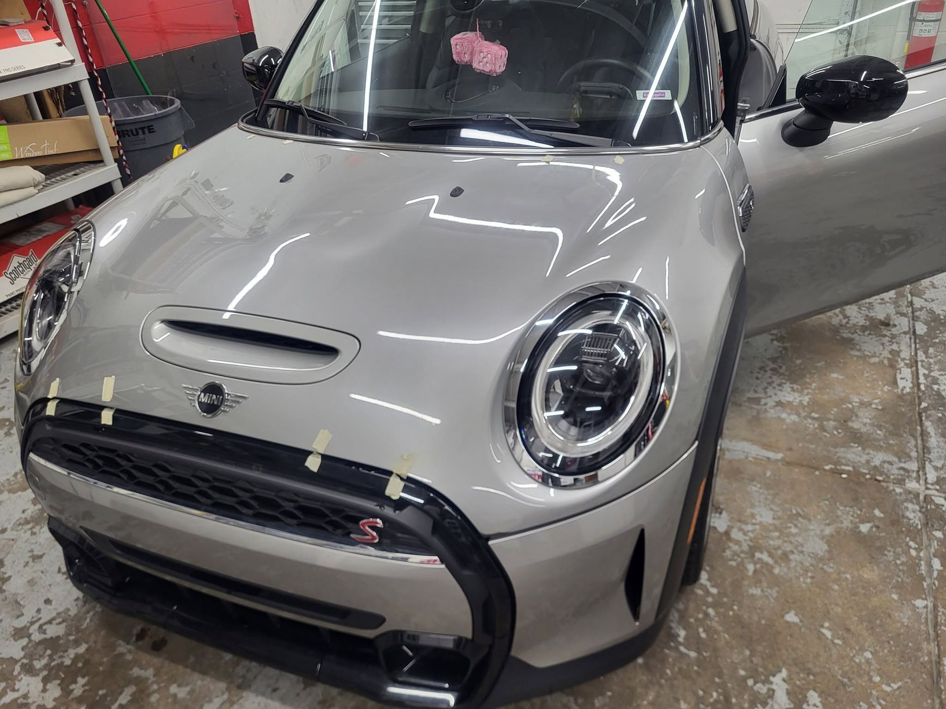 Silver Mini Cooper in a garage, front view with hood scoop and passenger door open.