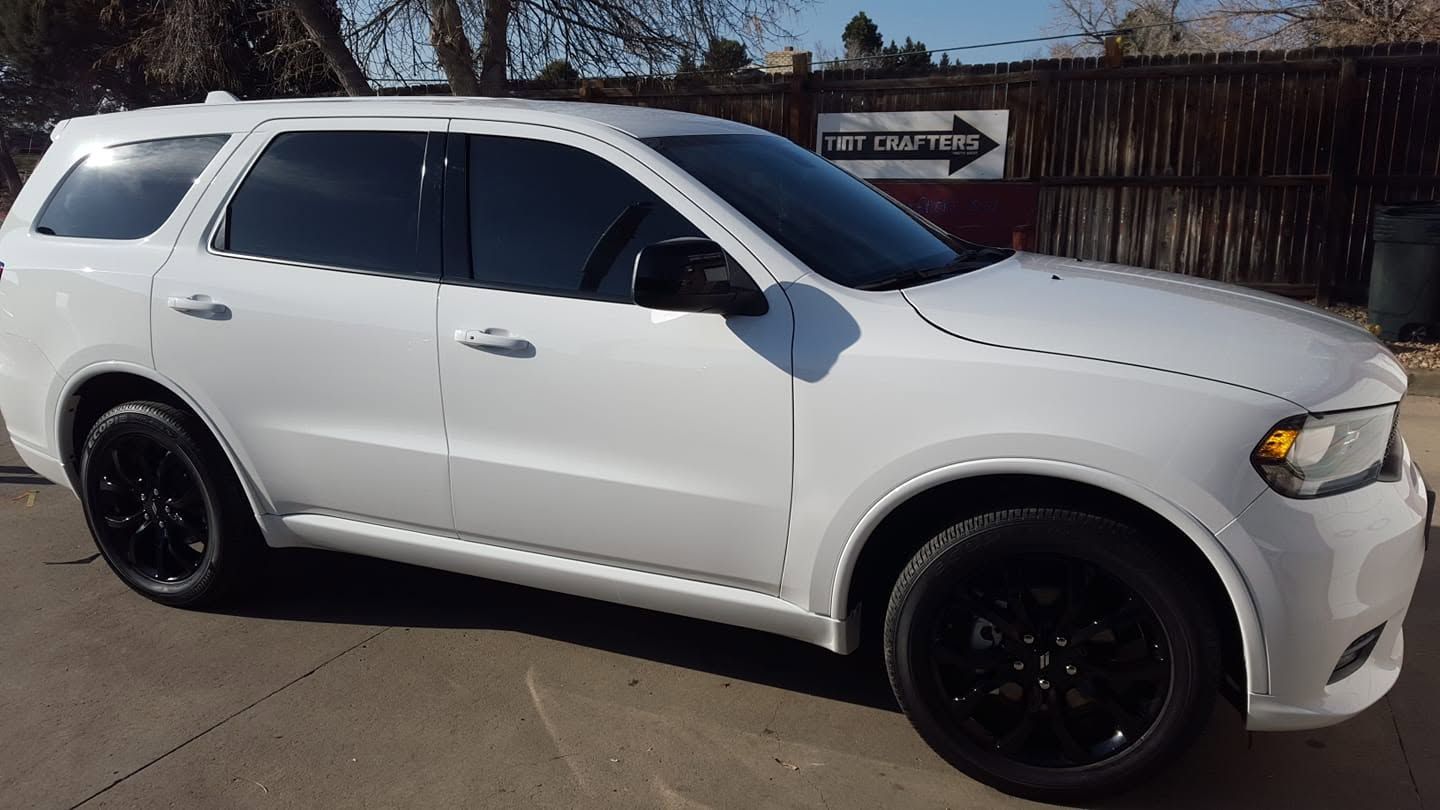 White SUV with black wheels parked outdoors in bright sunlight.