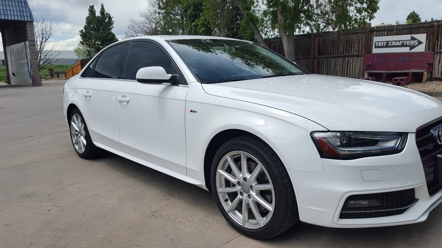 White sedan parked outdoors on a paved lot, side view with tinted windows.