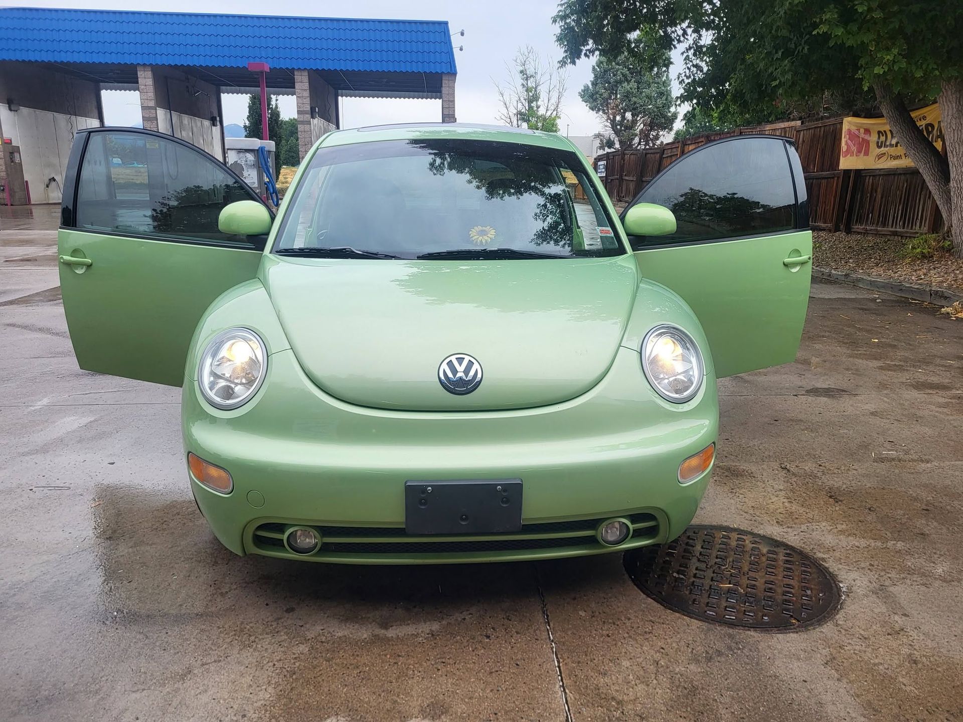 Light green Volkswagen Beetle with both front doors open, parked outdoors on a driveway.