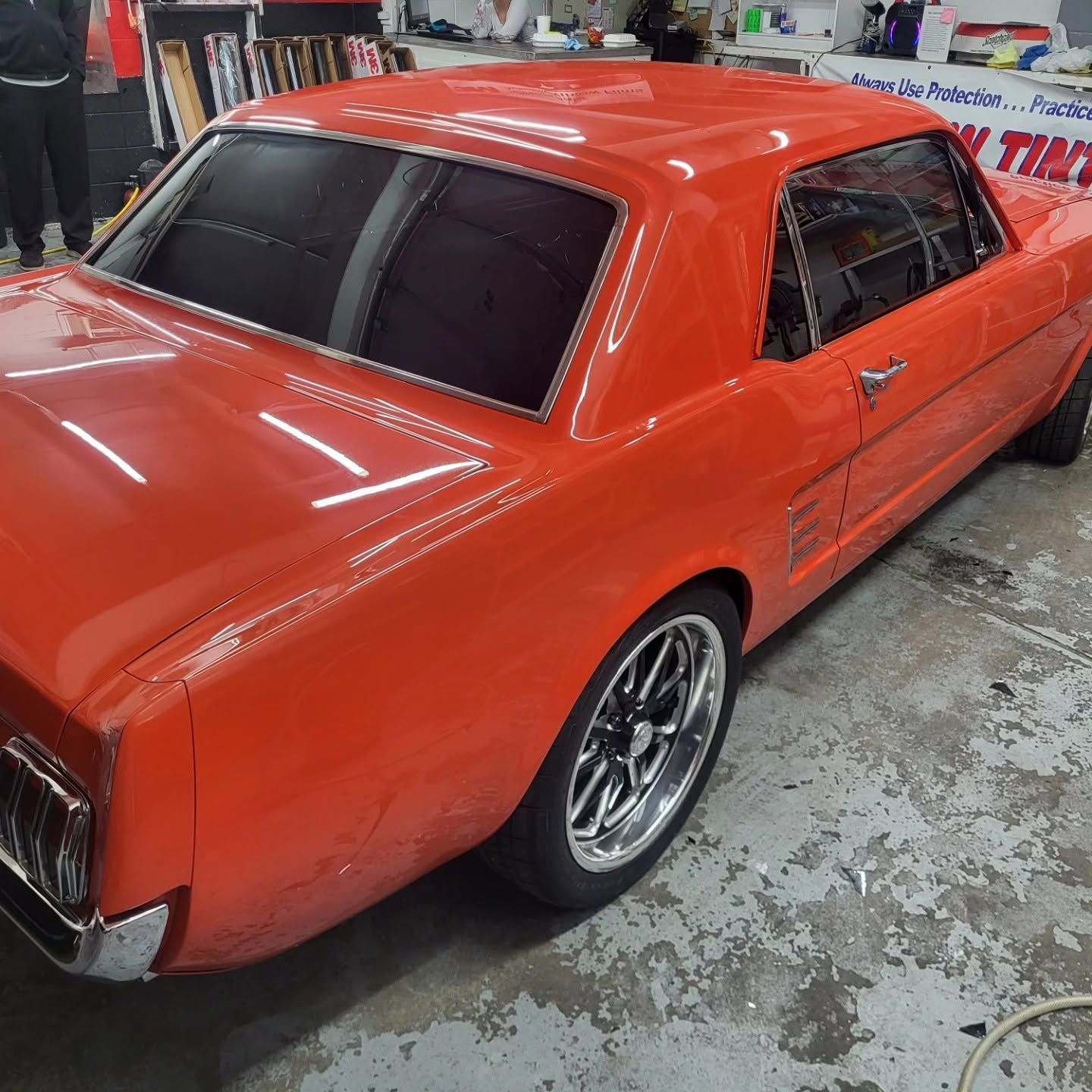 Orange classic car at an indoor auto show, viewed from the rear side.