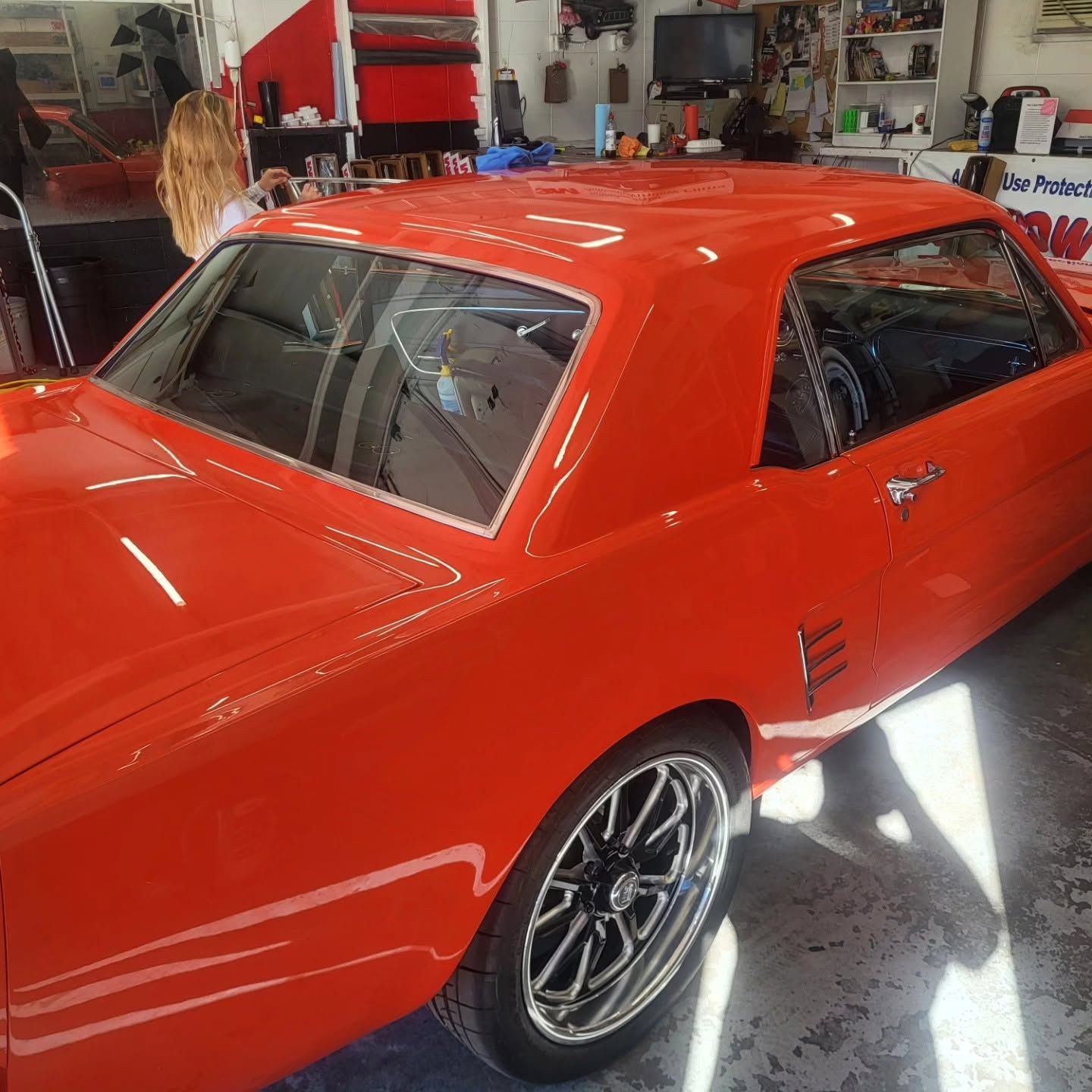 Red classic car in a garage, bright orange-red paint with black rims and a person in the background