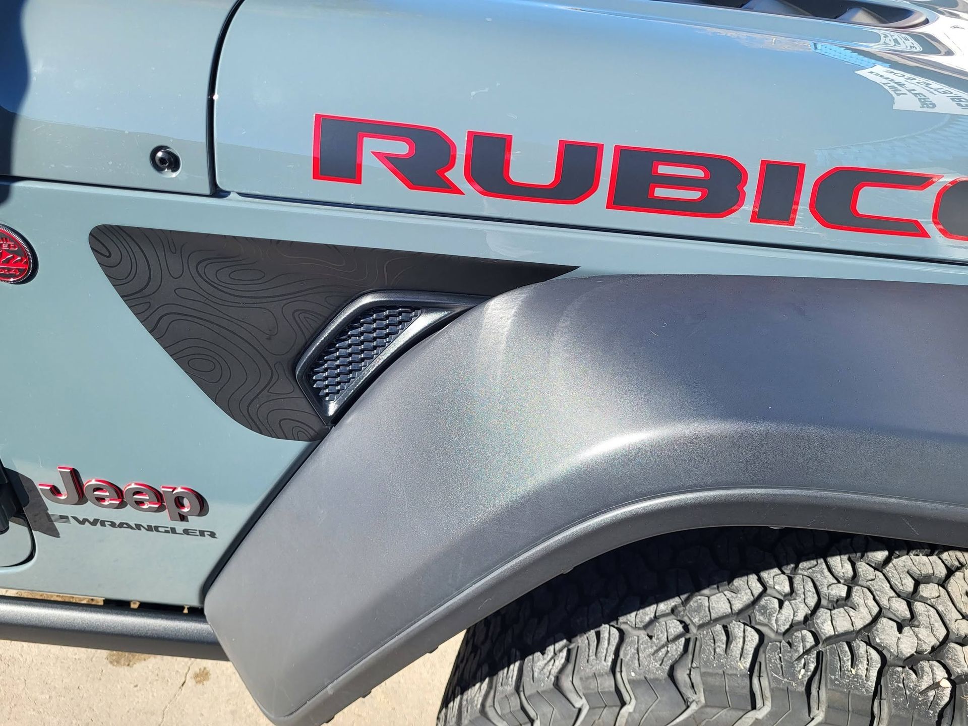 Close-up of a light blue Jeep Rubicon with black fender flare and rugged tire