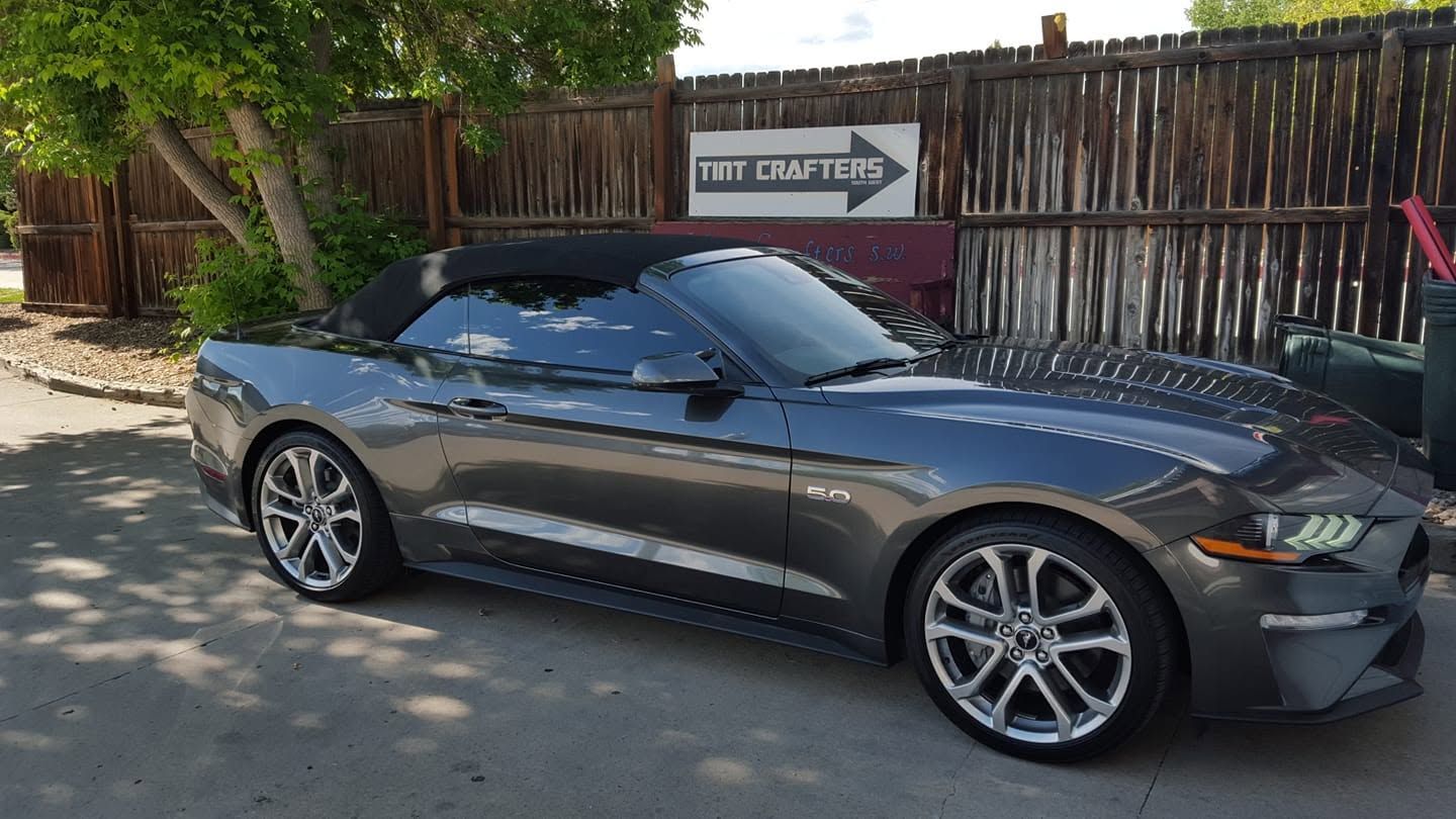 Gray convertible sports car parked by a wooden fence in front of a gate sign.
