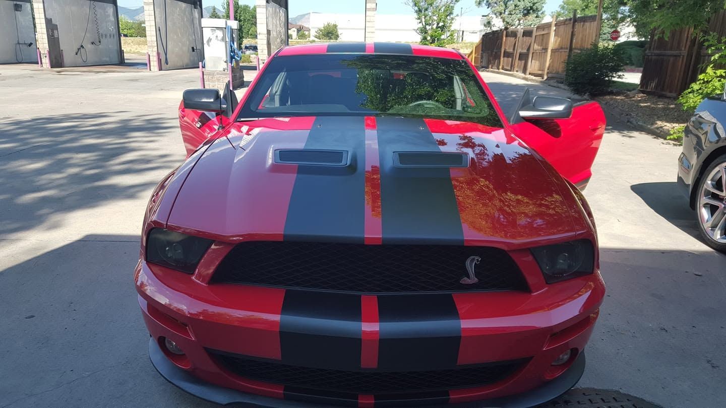 Red sports car with black racing stripes, front view on a street, driver doors open.