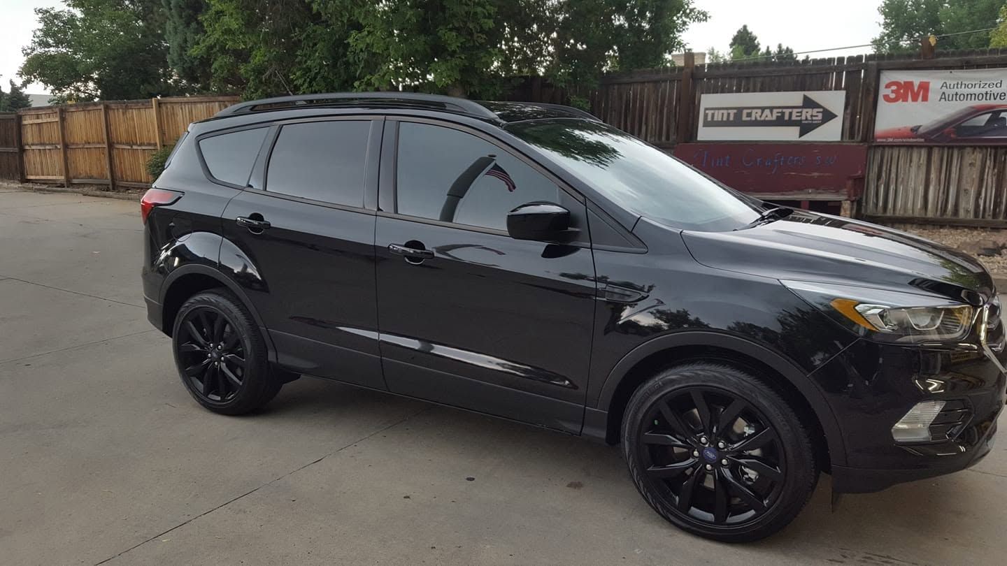 Black SUV parked on a concrete lot near a fence and trees.