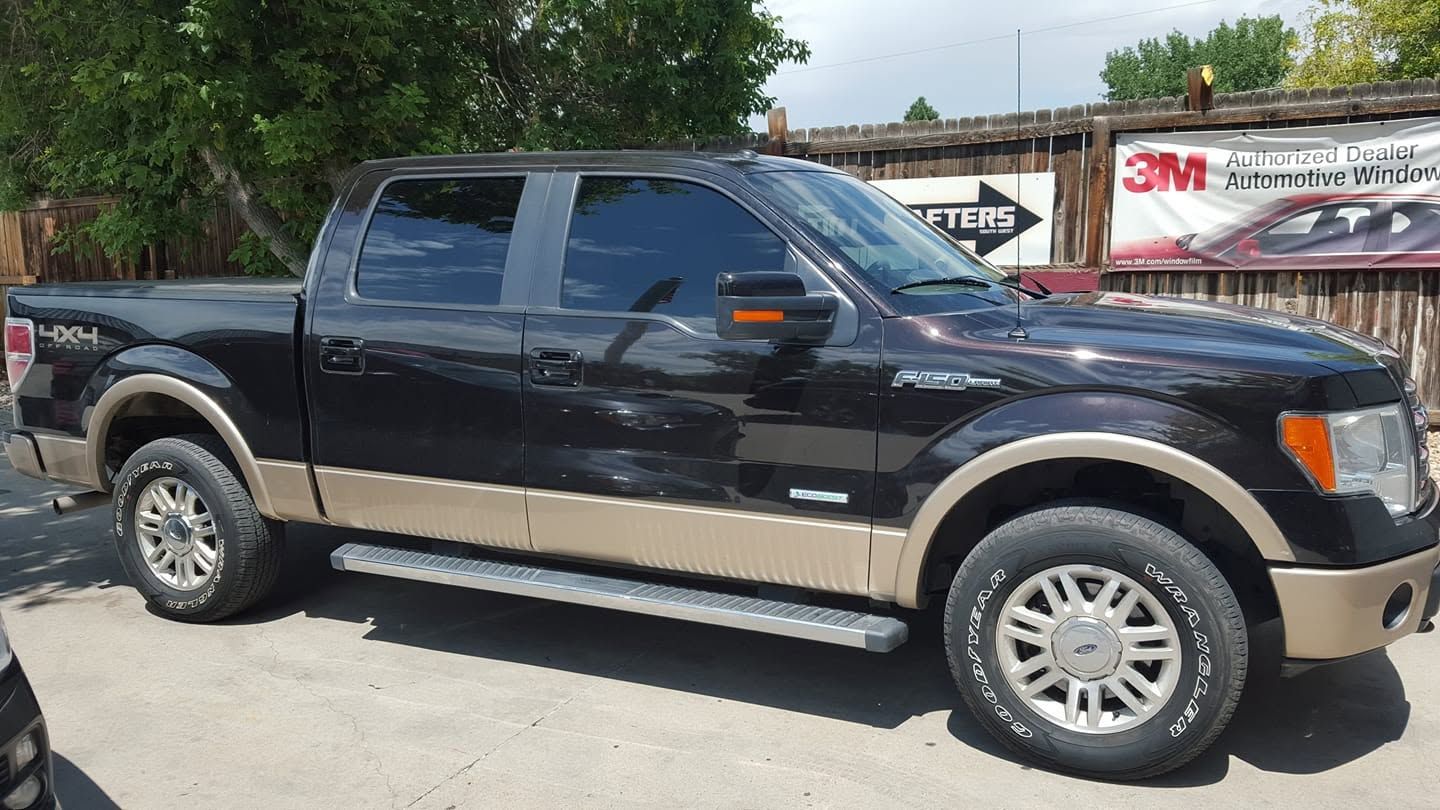 Black pickup truck parked outdoors beside a tree and building.