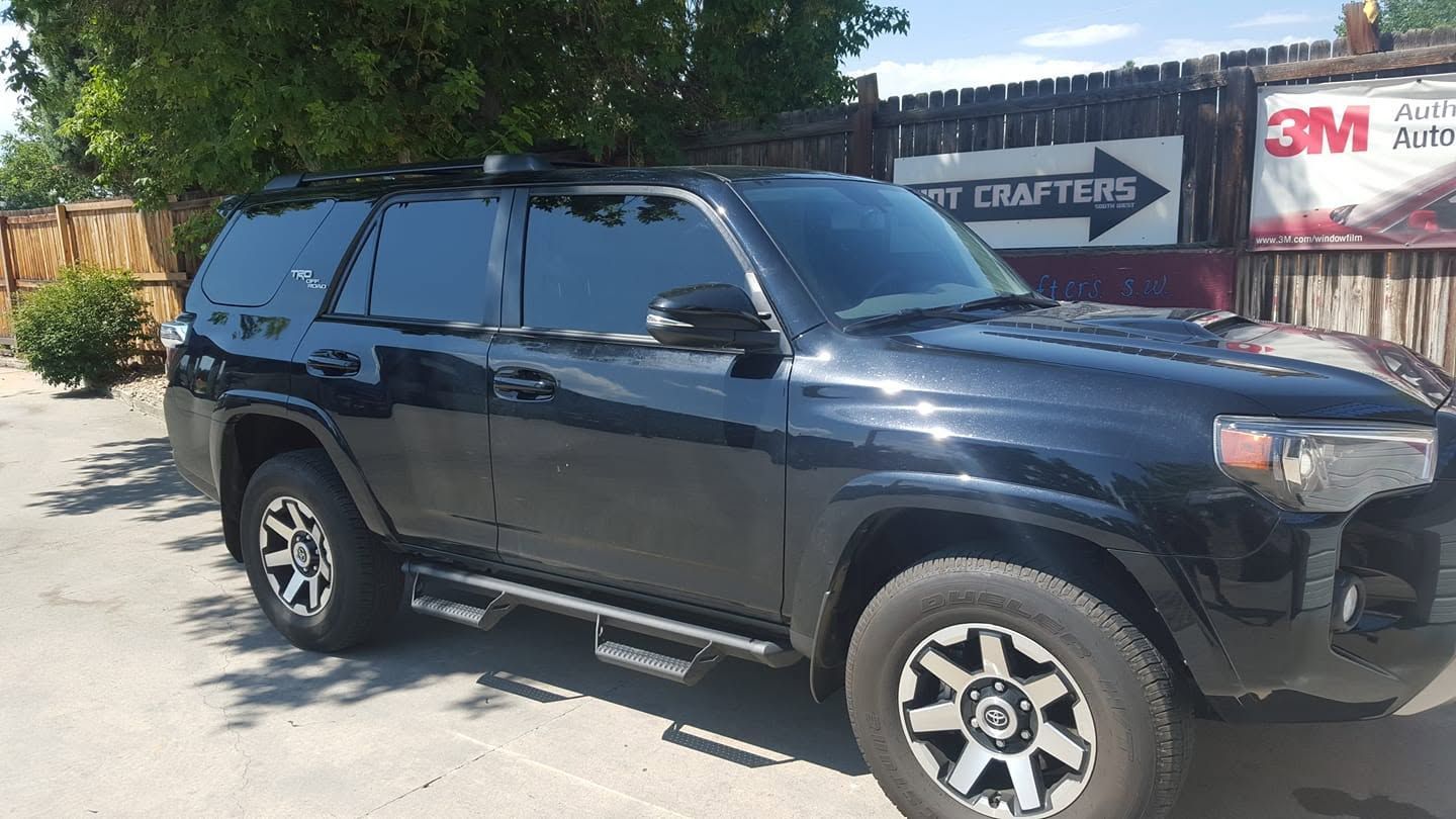 Black SUV parked outdoors near a building and fence in bright sunlight
