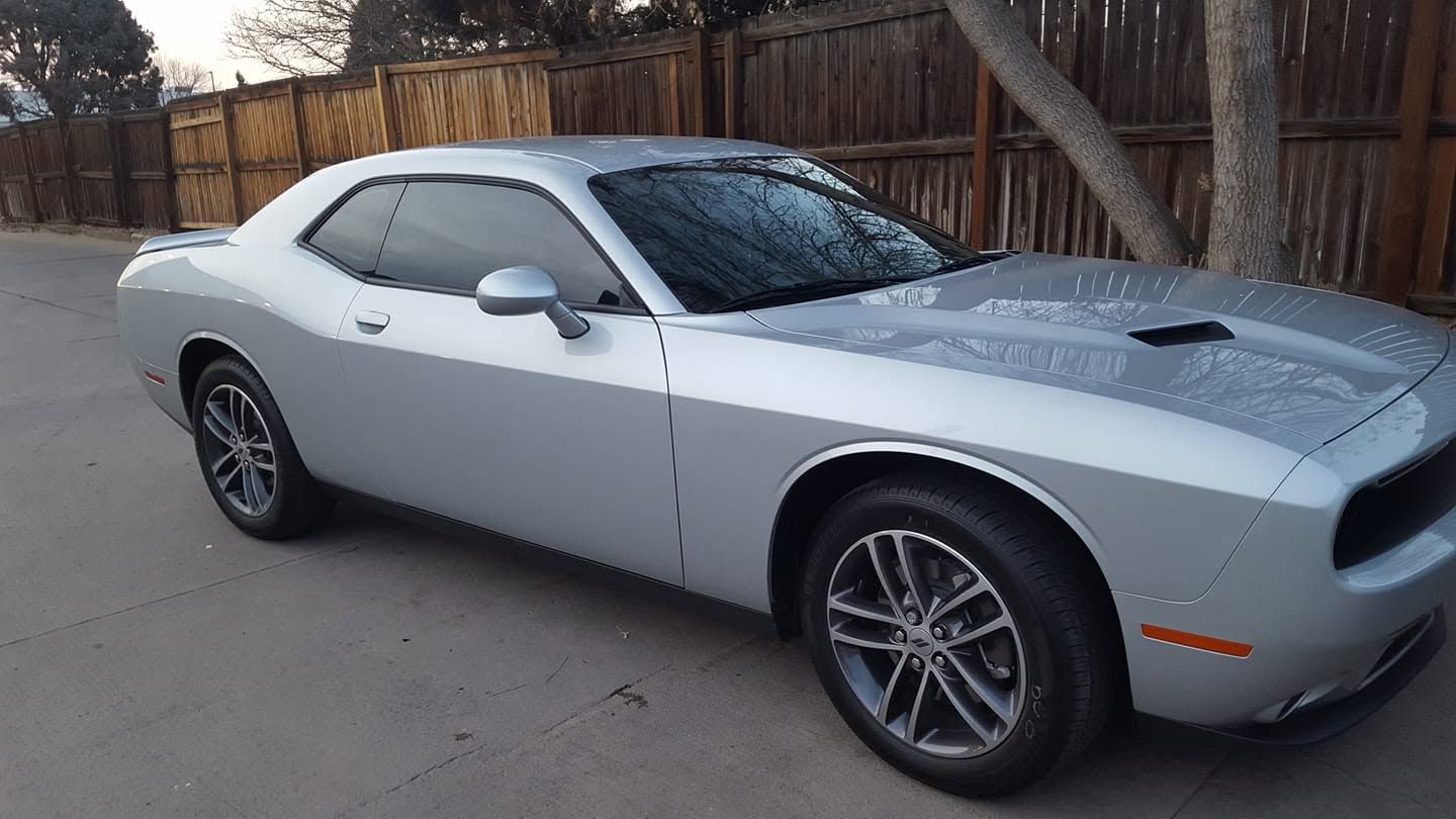 Silver sports car parked on a driveway beside a wooden fence