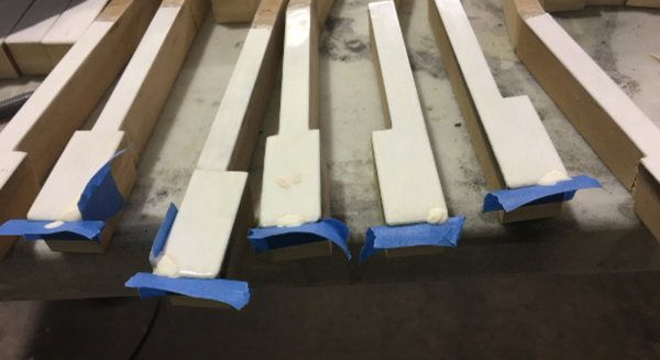 Close-up overhead view of piano keys in various stages of restoration, showing cream-colored ivory or synthetic keytops