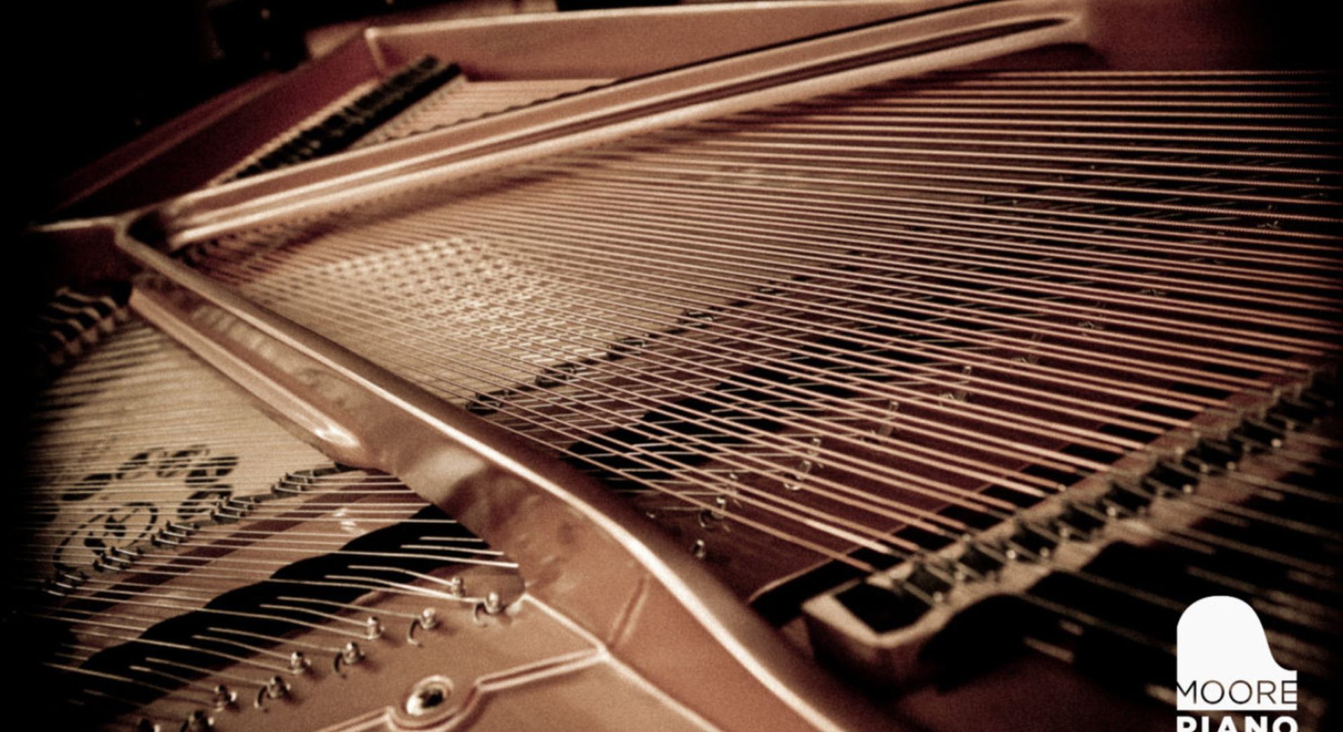 Interior detail of an open grand piano showing the harp frame, strings, and wooden soundboard with decorative scrollwork