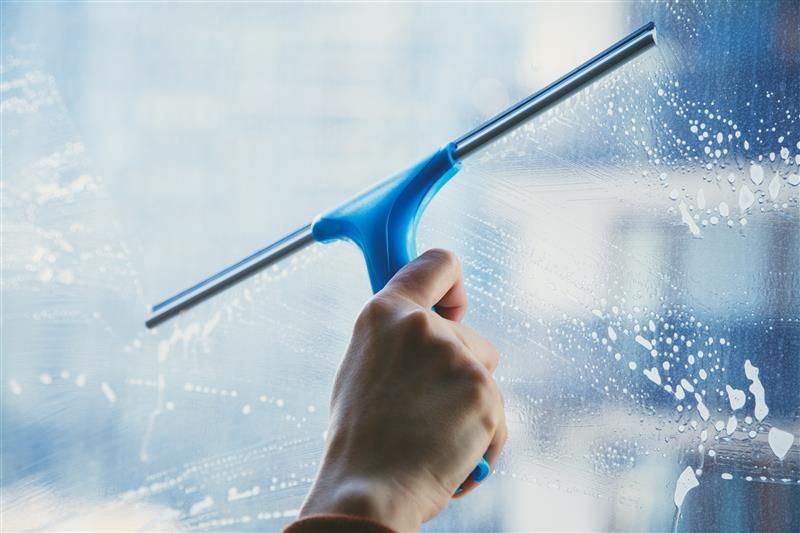 Person in yellow gloves cleaning a window with blue cloth and spray bottle.