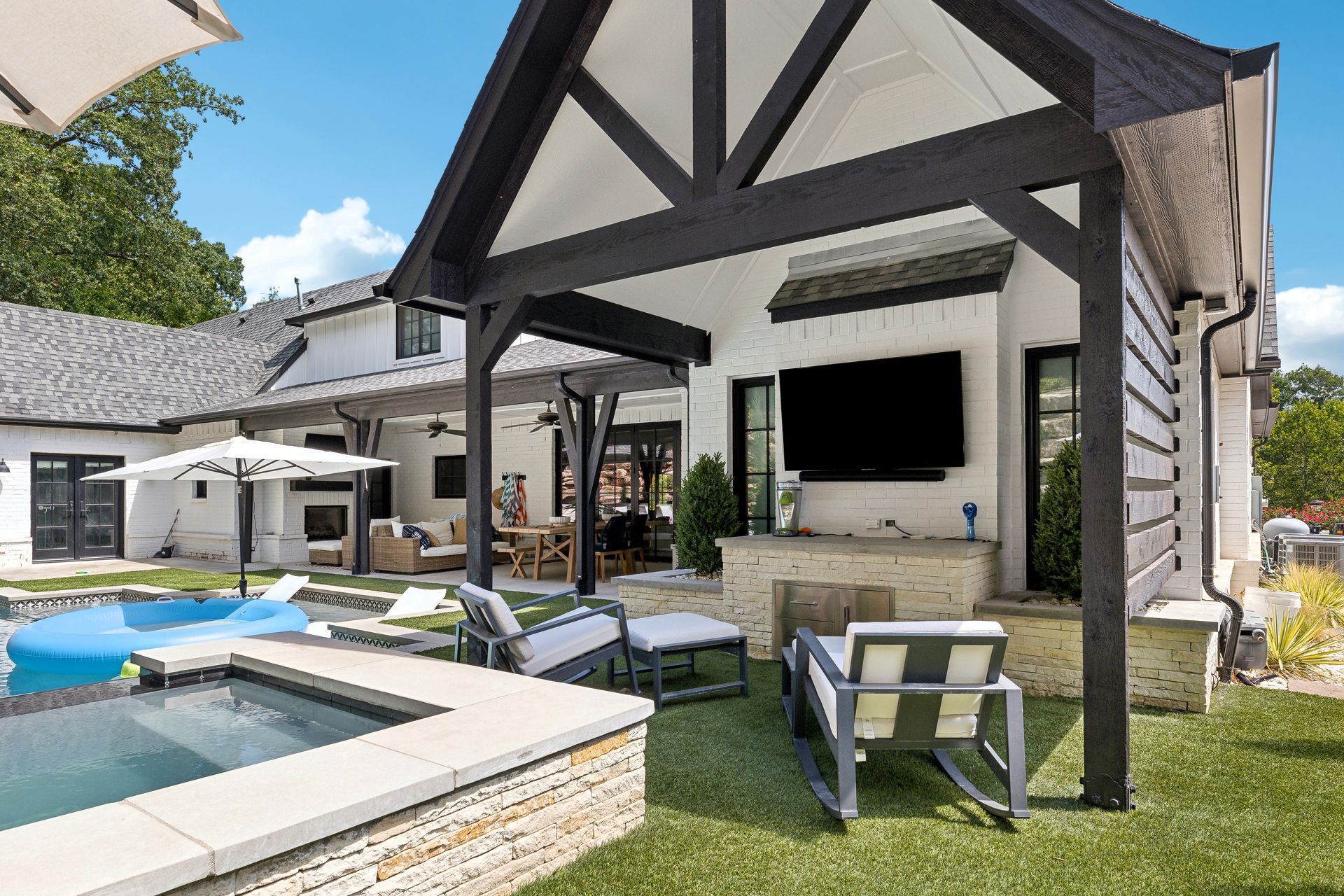 Backyard with pool, patio, outdoor TV, seating, and white house.